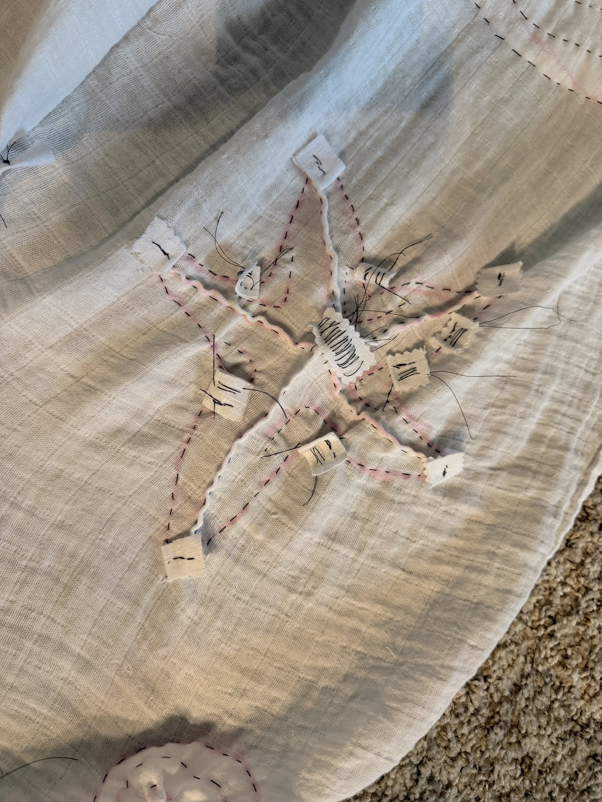 A starfish resist design stitched in black.  The outline, spines, and small curved lines are visible, as well as tabs to secure the ends of threads.