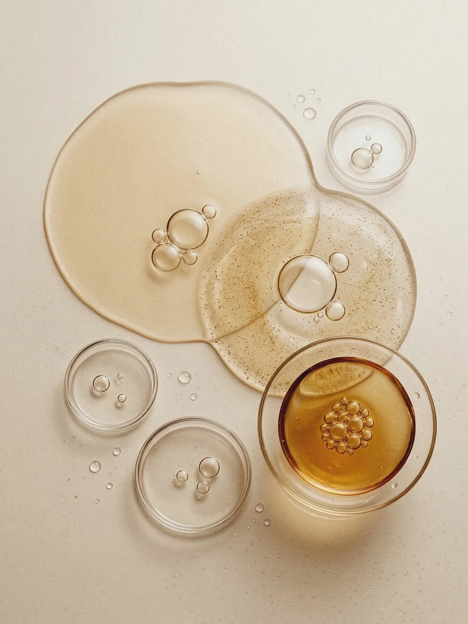 Various drops of oil and liquids in glass bowls on a white surface.