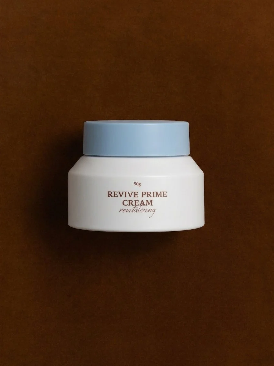 A white cosmetic jar with a light blue lid labeled 'Revive Prime Cream revitalizing' on a brown background.