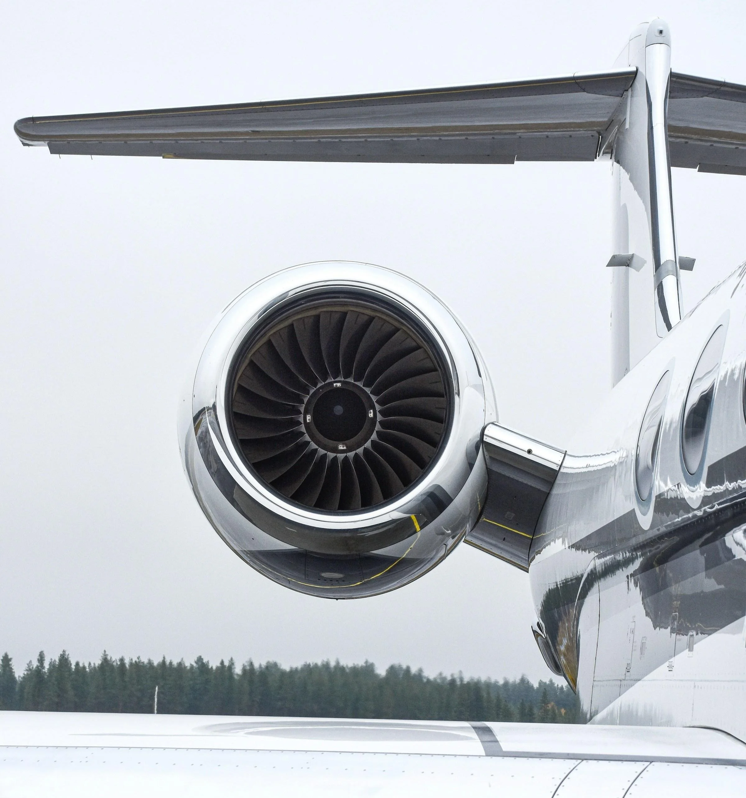 Close-up of a jet engine mounted on the wing of an airplane with a forested landscape in the background.