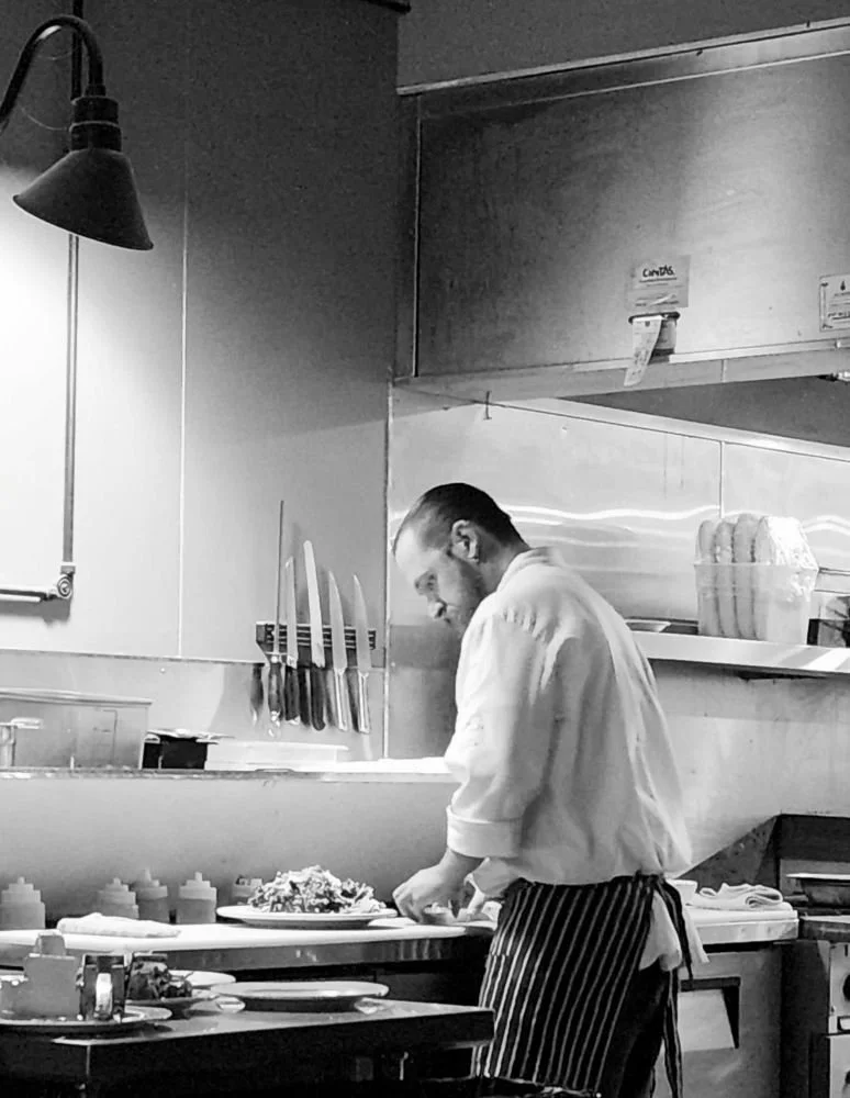 A chef with a striped apron working in a professional kitchen, preparing food.