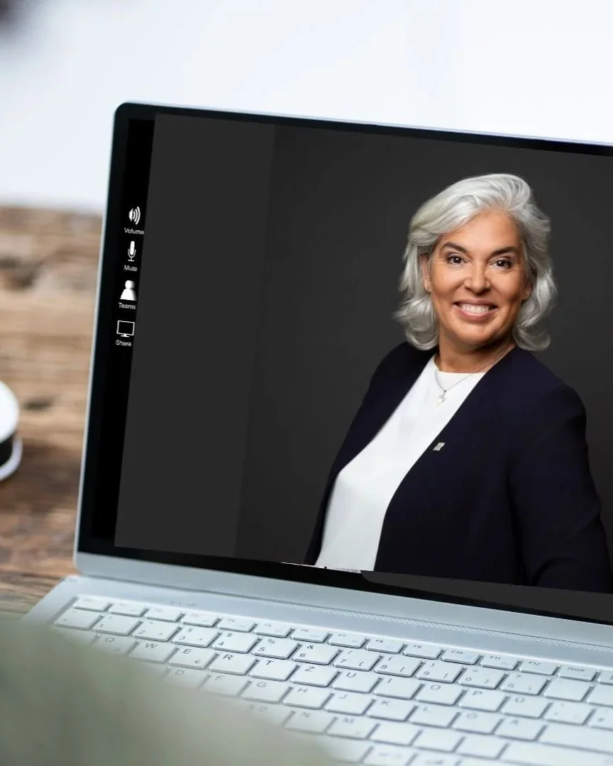 A woman with gray hair smiling during a virtual meeting on a laptop.