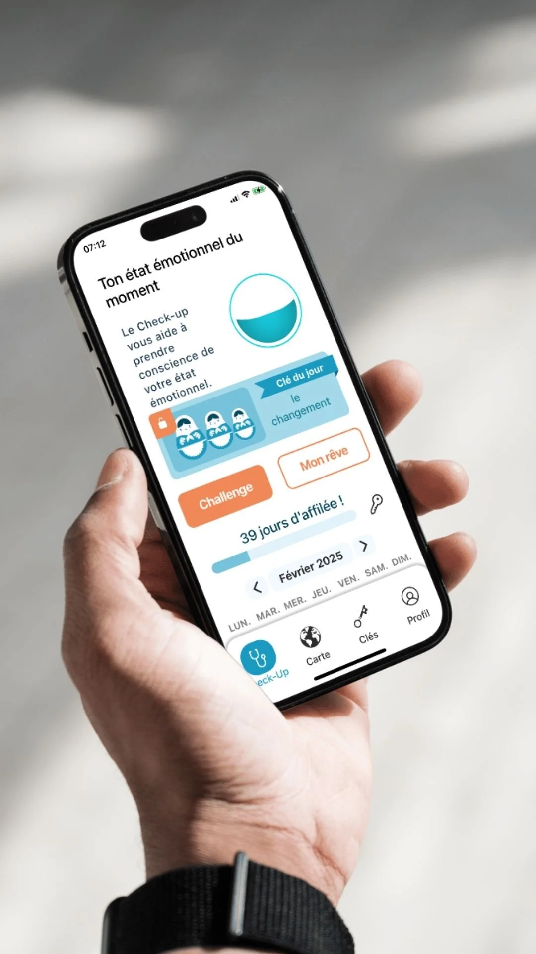 A person holding a smartphone displaying an app in French that tracks emotional and mental health, showing a mood indicator, a challenge button, and a calendar with the current date in February 2025.