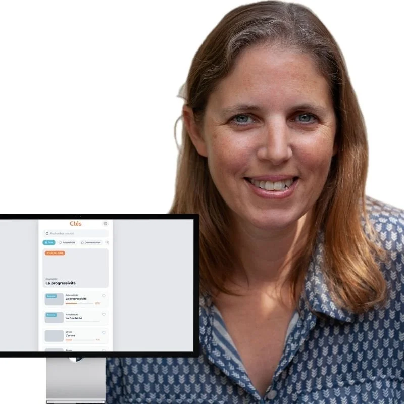 A woman with light brown hair and a blue patterned shirt smiling, with a computer monitor showing a language learning app in front of her.