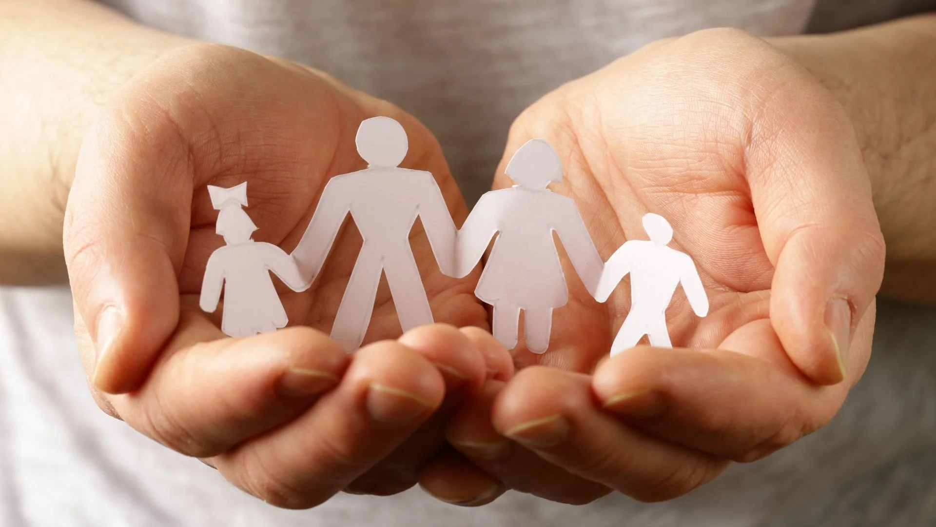 Hands holding paper cutouts of a family of four, representing a mother, father, and two children.