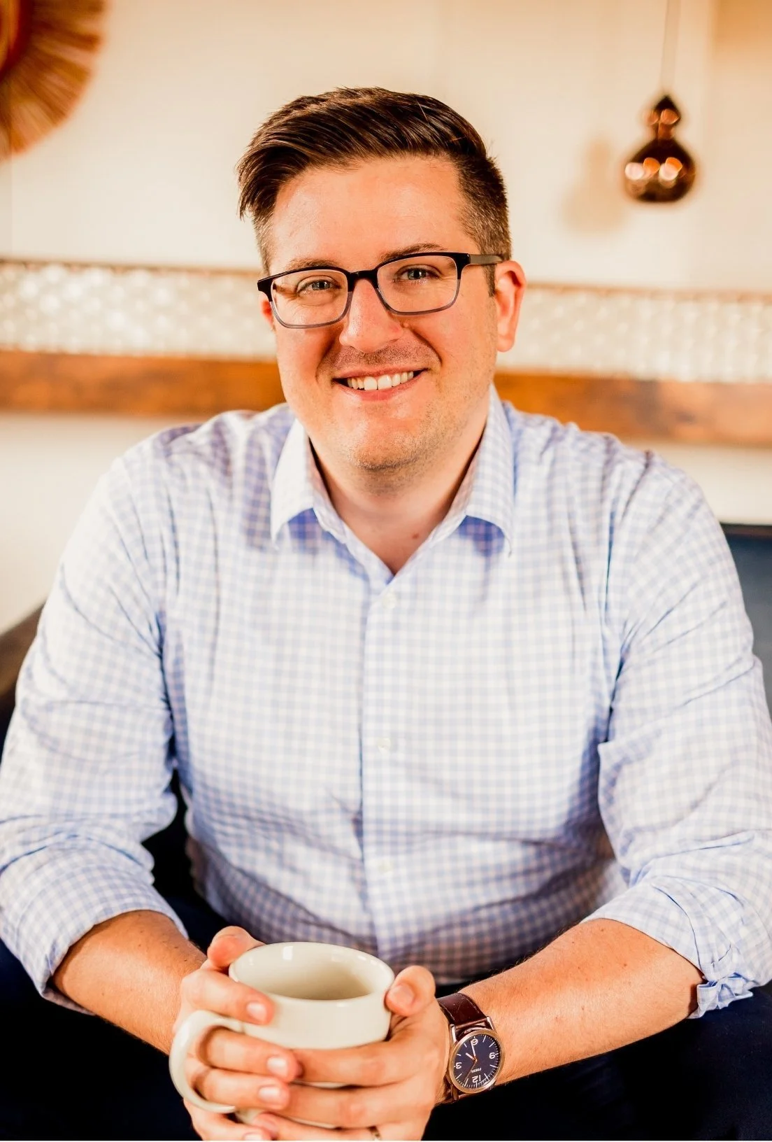 Joe Burke, a Charlotte therapists, sits smiling while holding a white mug.