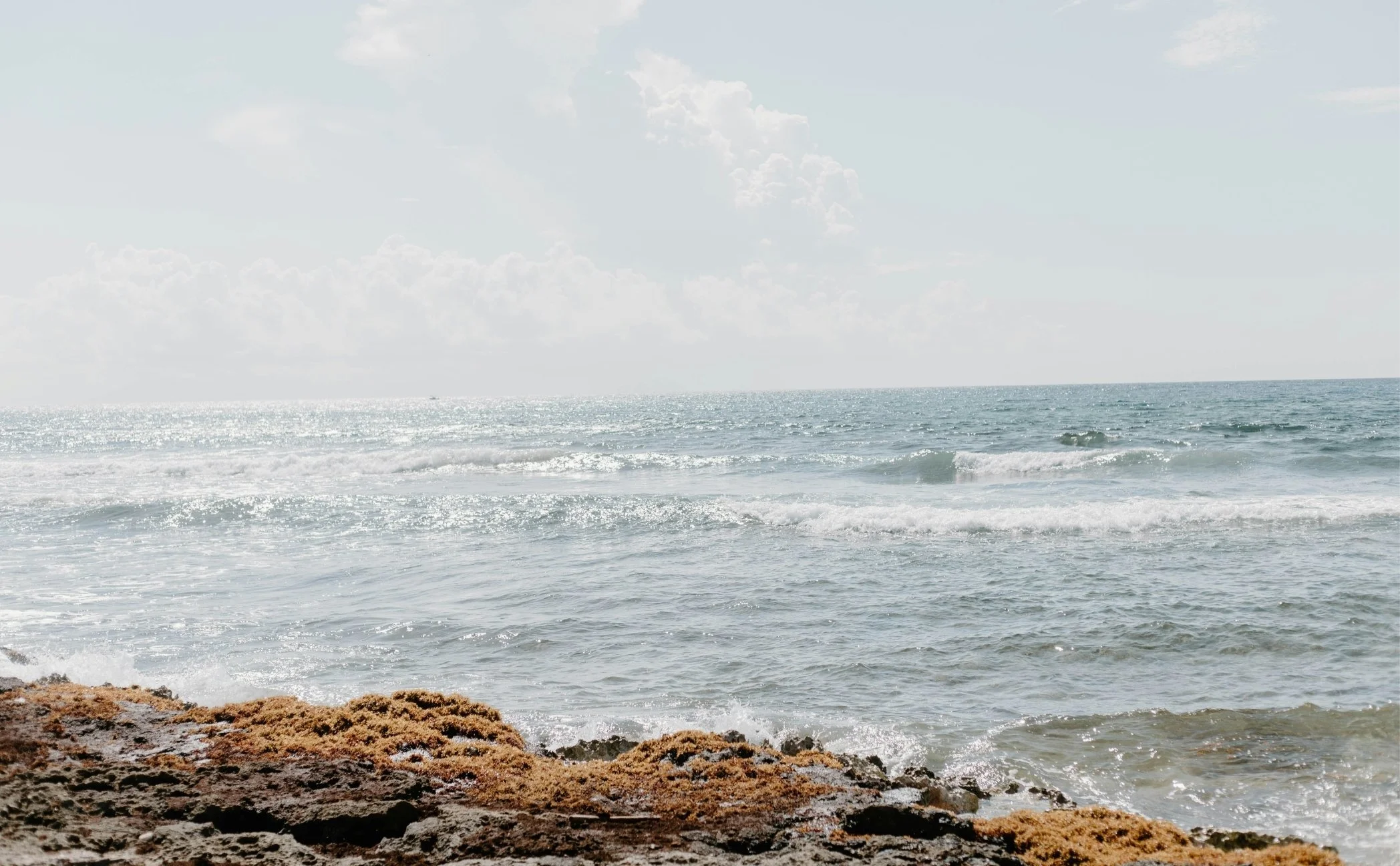 Coastal scene with ocean waves and rocky shoreline under partly cloudy sky.