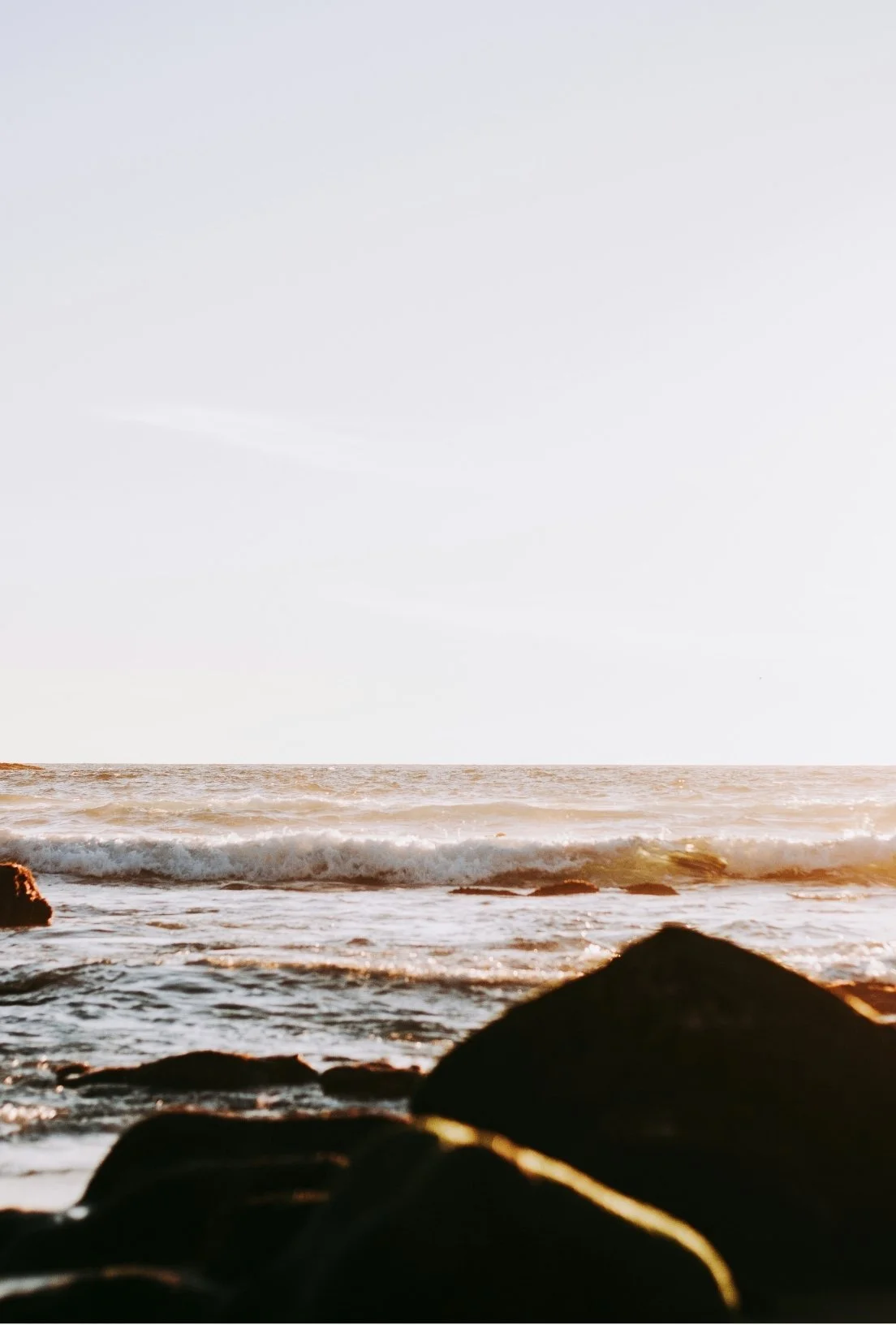 A photo of a sandy beach with rocks and ocean waves during sunset or sunrise.