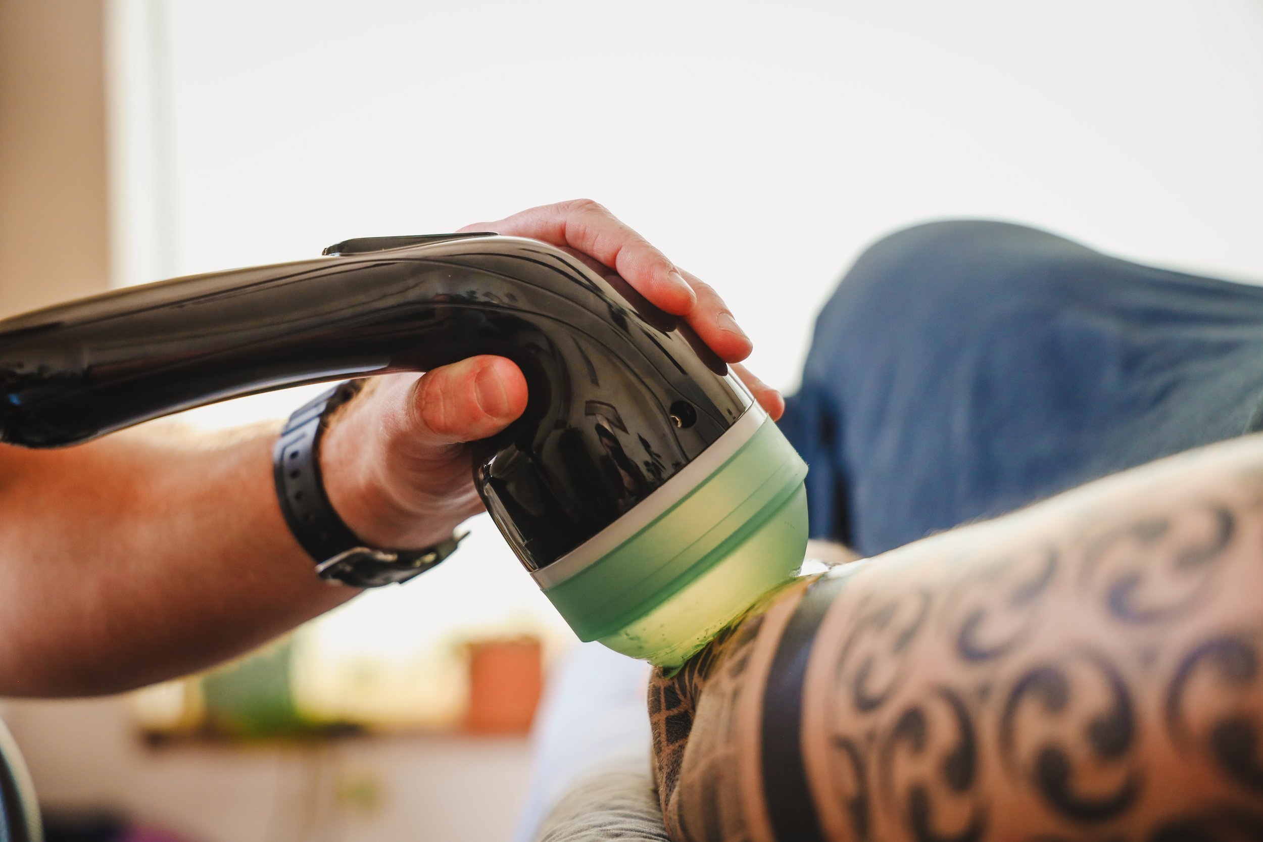 Close-up of a person’s hand holding a can, with tattooed arm visible, pouring or applying something onto a colorful surface