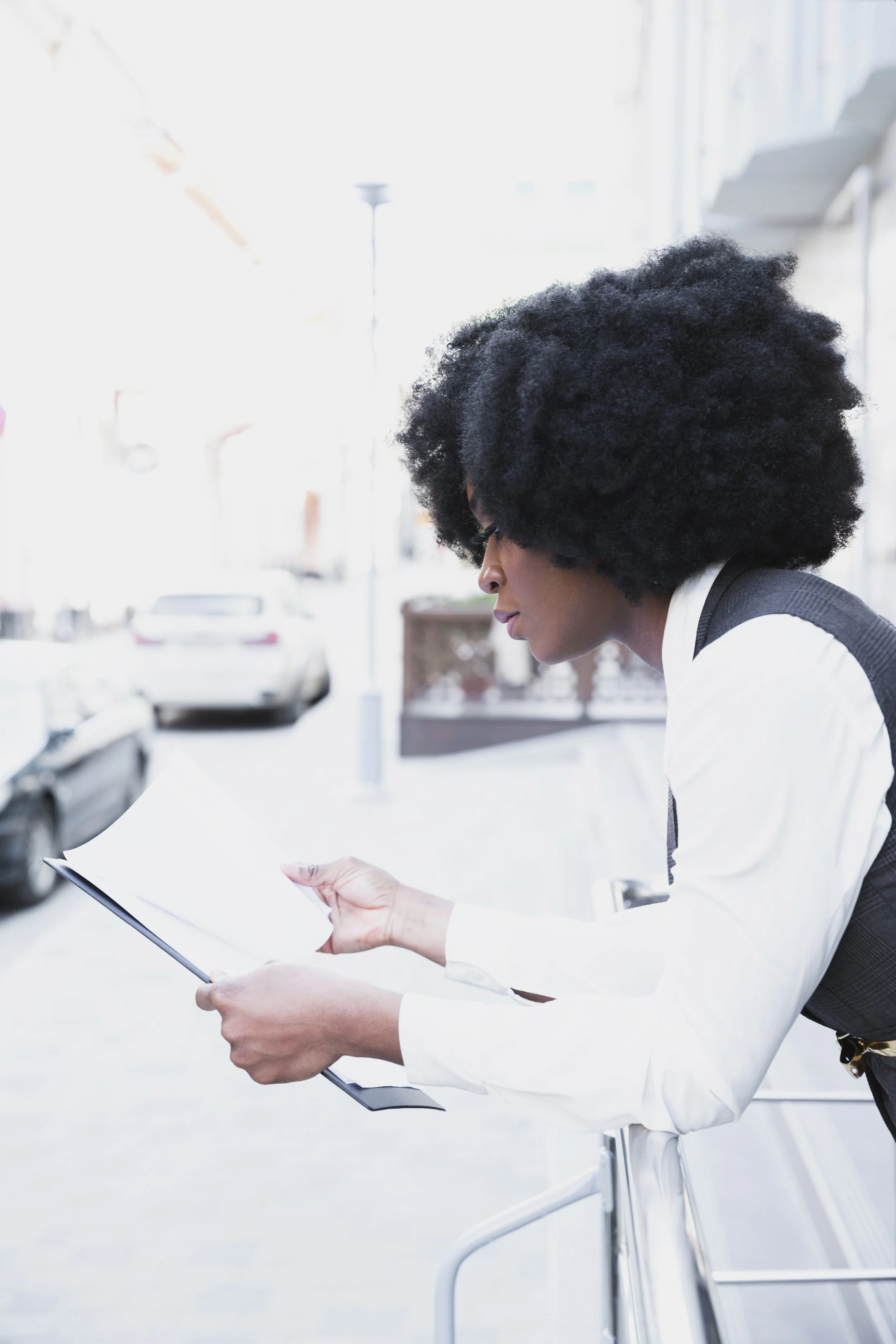 young-african-businesswoman-leaning-railing-reading-document-paper