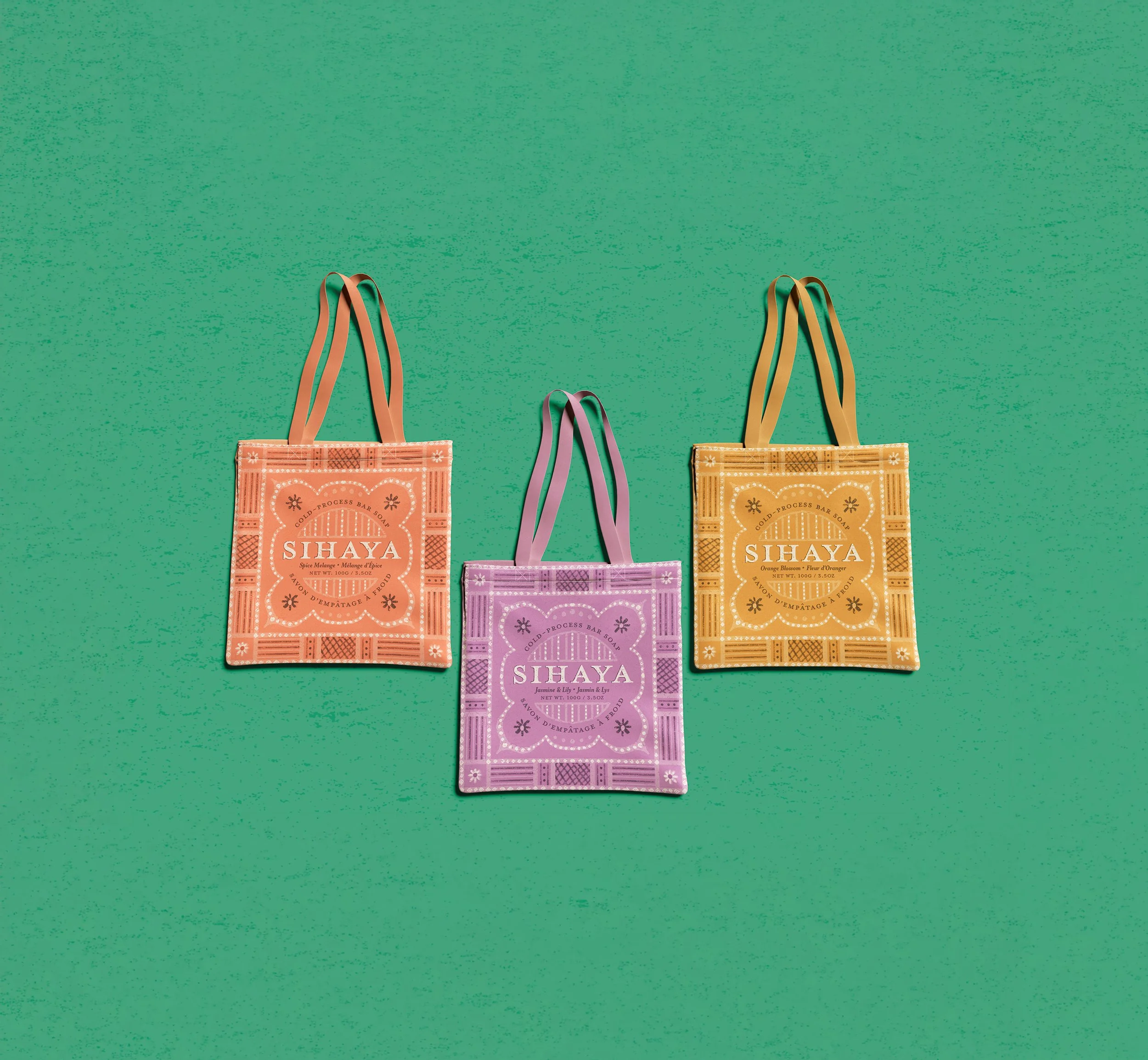 Three colorful tote bags with floral and geometric patterns, labeled 'SIHAYA', laid on a green textured surface.