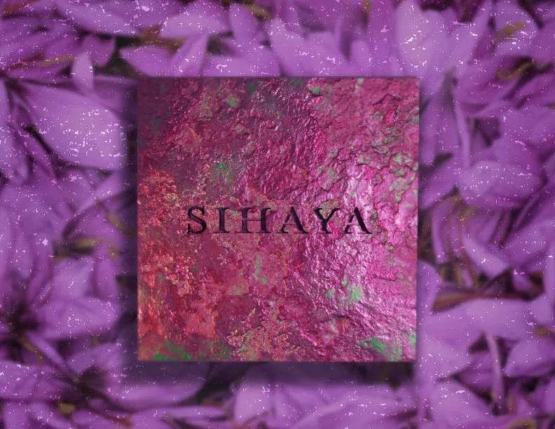 A textured pink and purple box with the word 'SIHAYA' on it, placed on a background of purple flower petals.