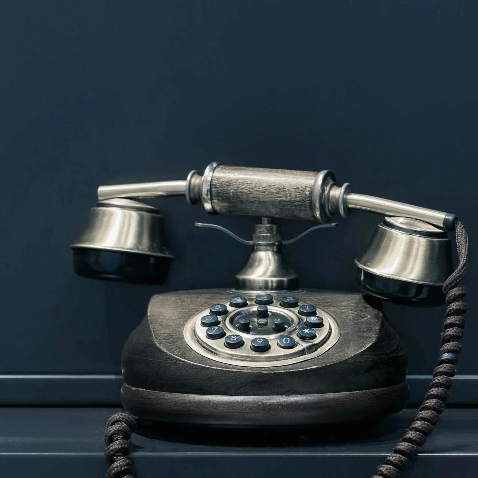 Vintage rotary telephone with a wooden handle as the receiver, set against a dark background.