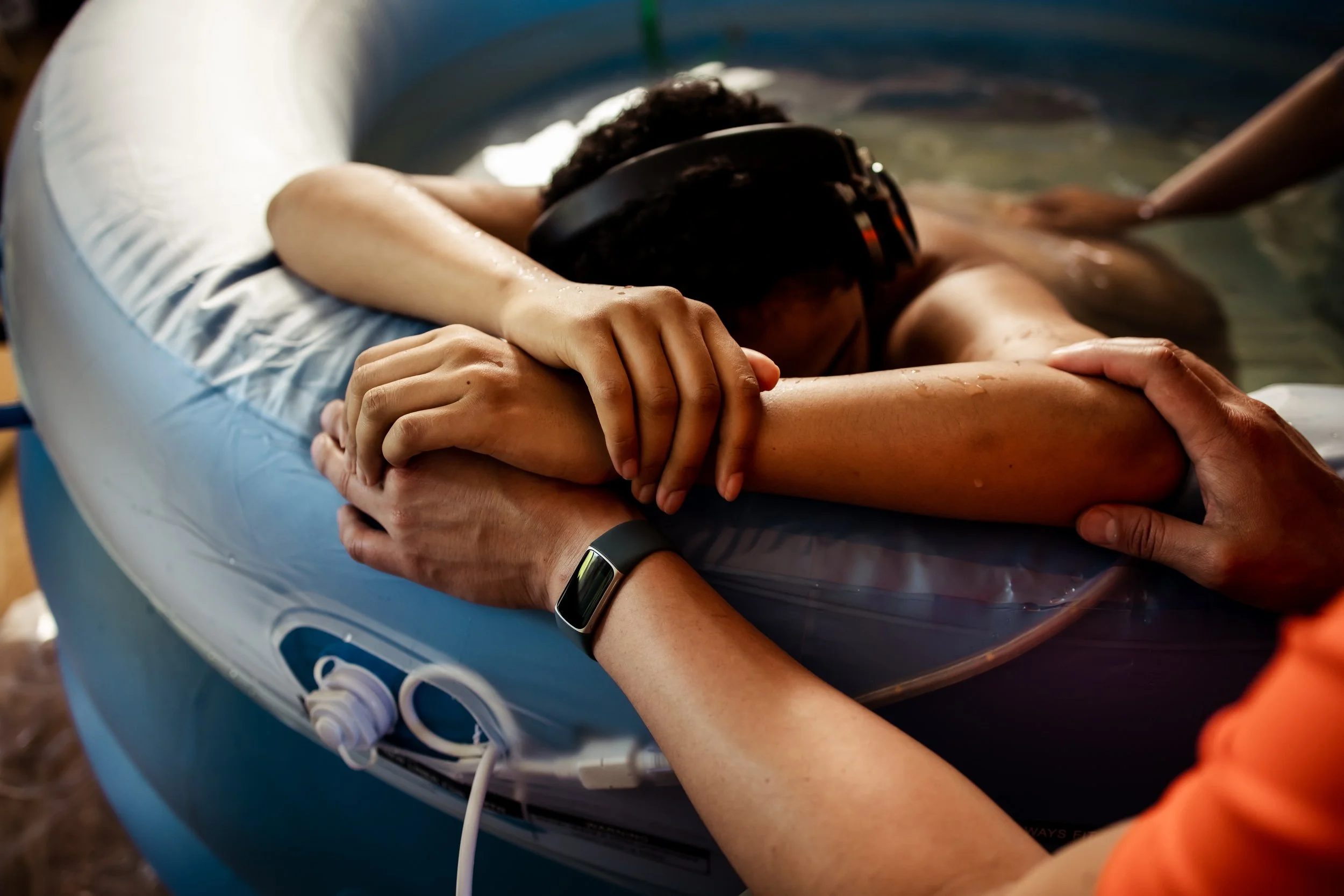 Person being baptized in a small inflatable pool, with a person holding their arm during the baptism.