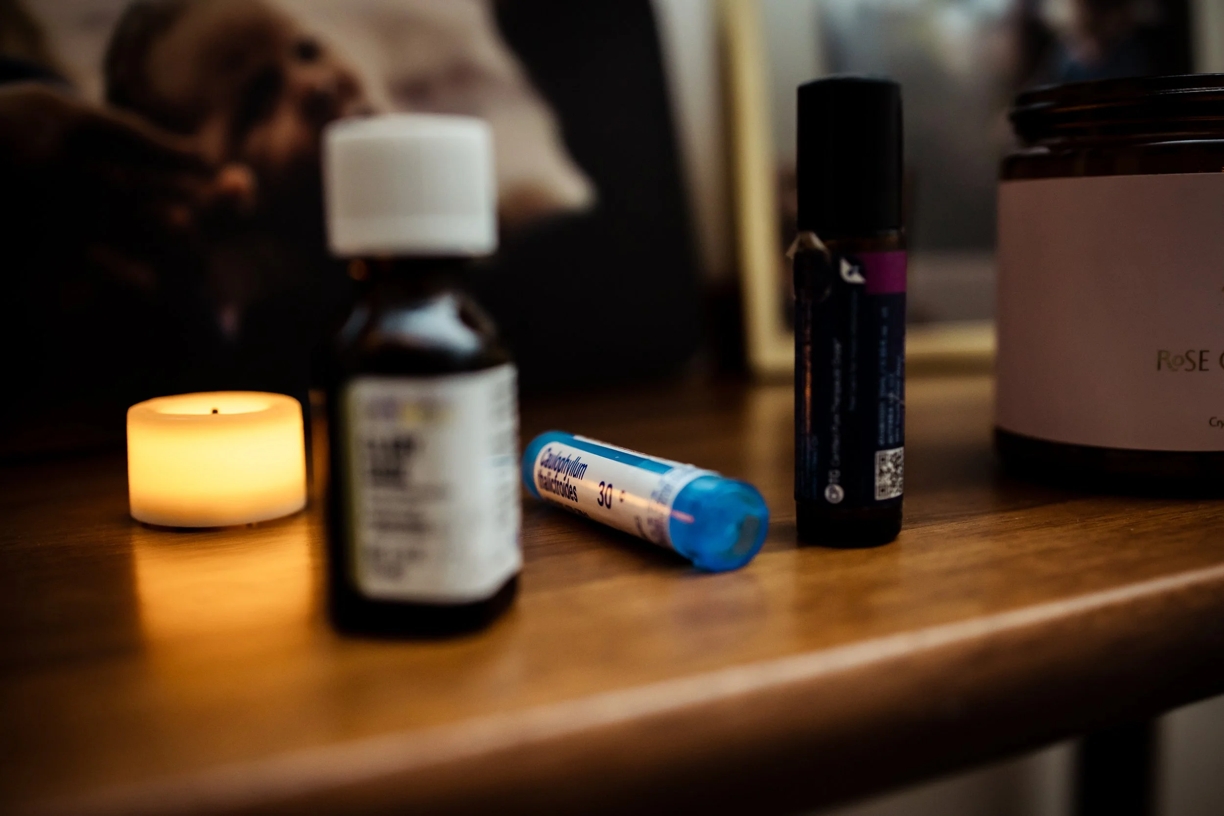 Various medication bottles and a temperature thermometer on a wooden surface with a lit candle in the foreground.