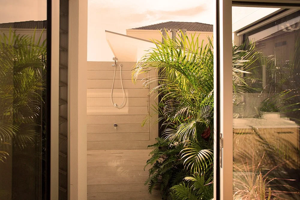 Outdoor shower area with lush green plants and a sliding glass door.