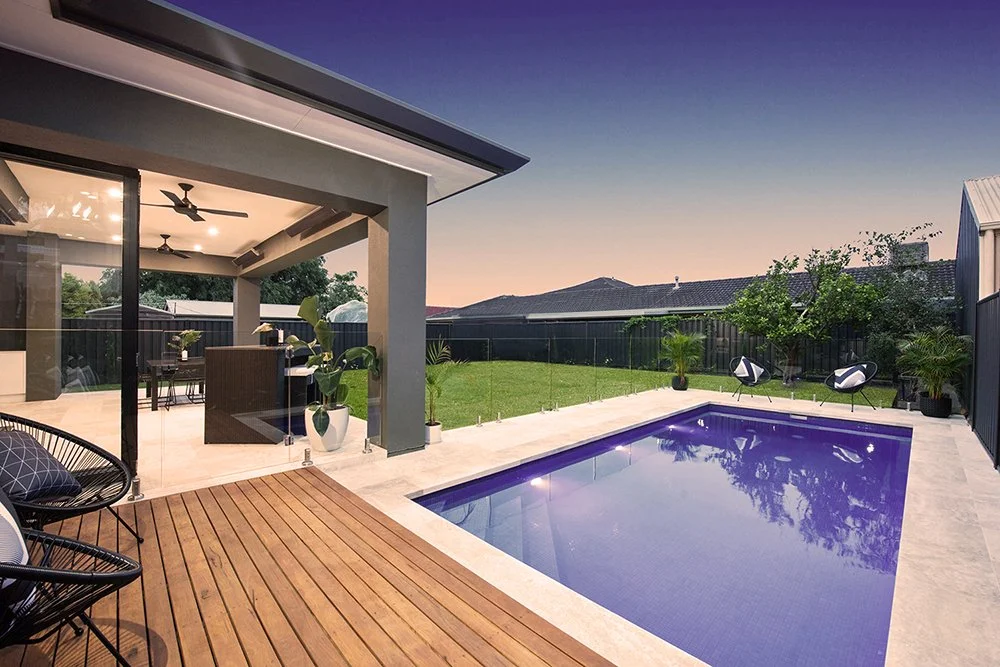 Modern backyard with a swimming pool, wooden deck, outdoor seating, and a covered patio area with ceiling fans and potted plants.