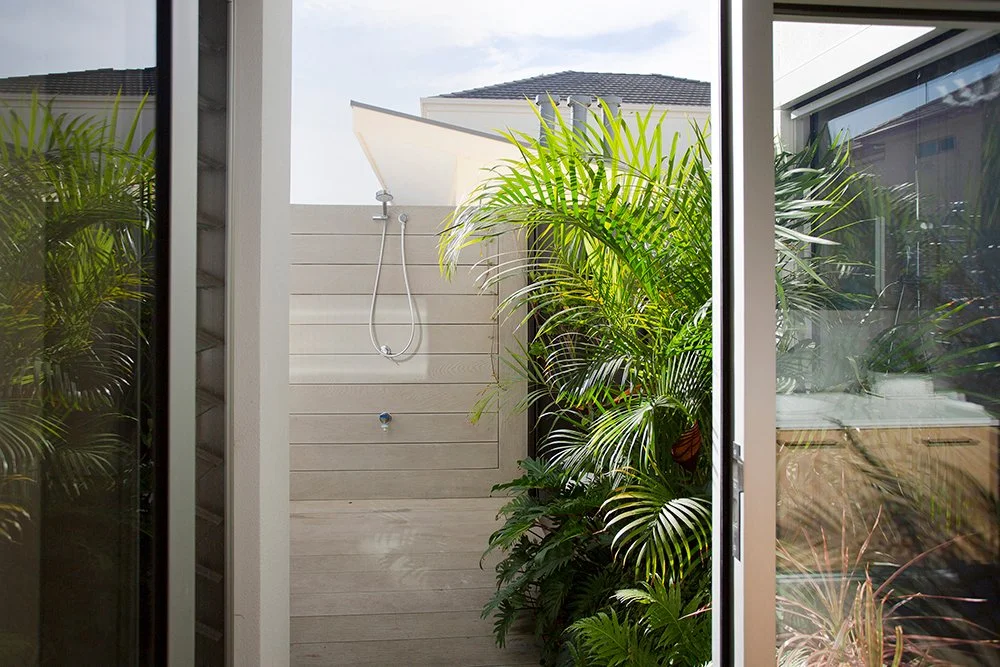 Outdoor shower area with lush green plants and a sliding glass door.
