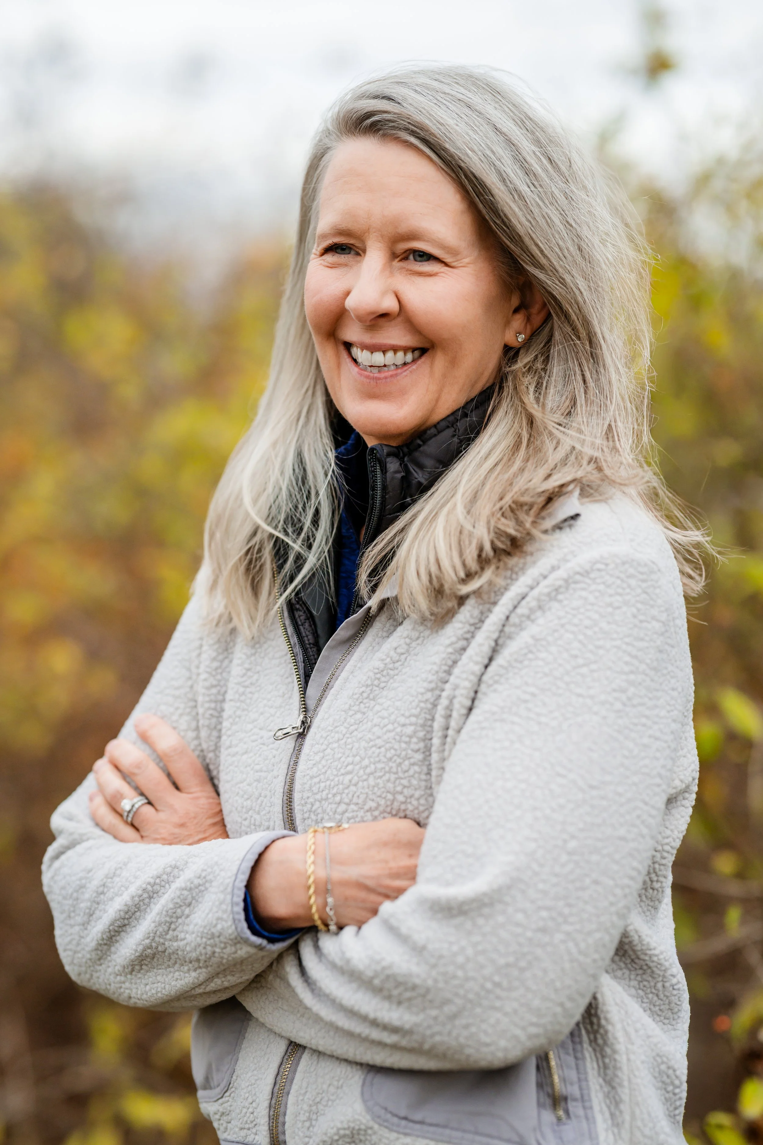Headshot of Clara Bowron smiling with a gray sweater and fall foliage in the background