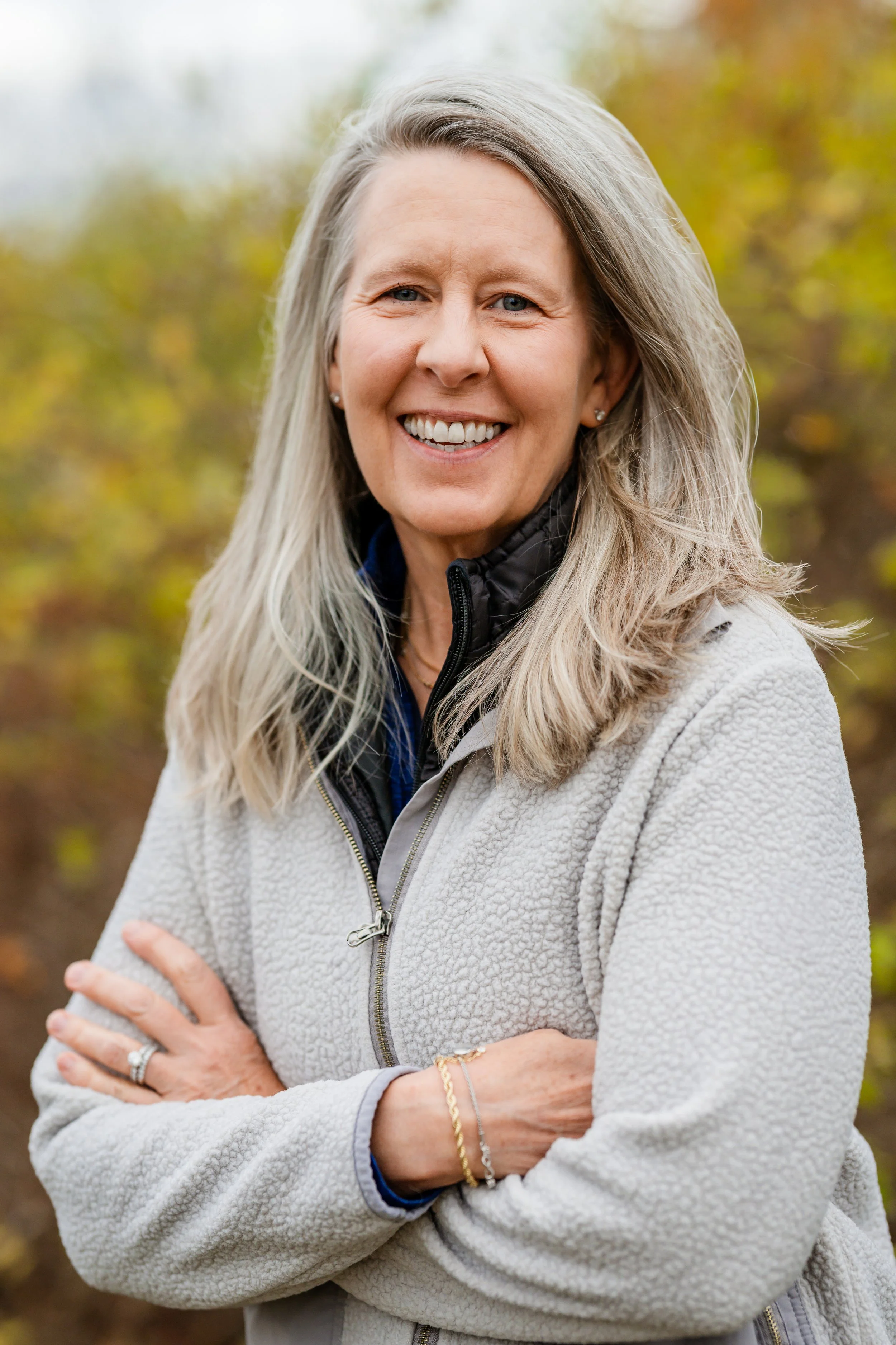 Headshot of Clara Bowron smiling with a gray sweater and fall foliage in the background