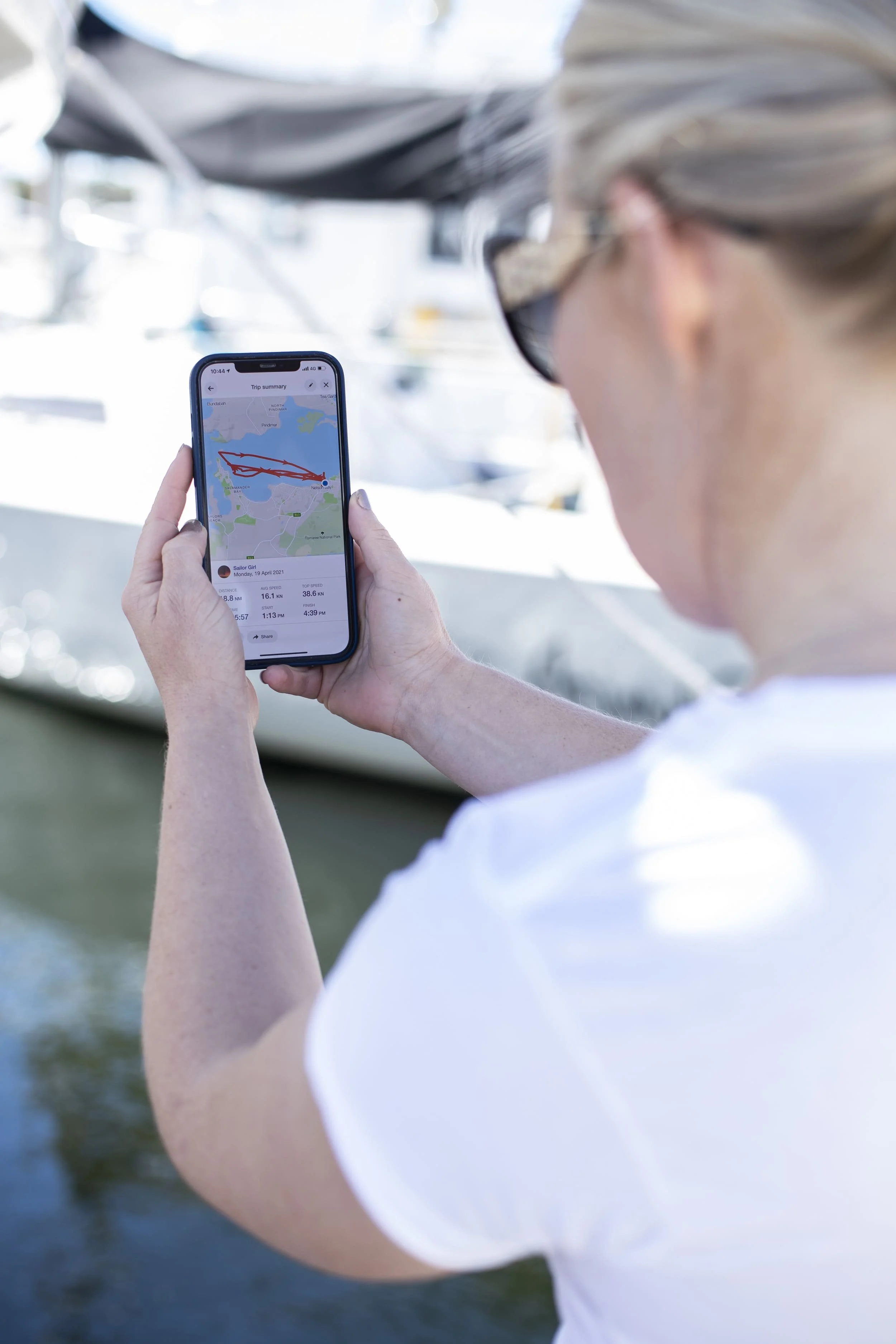 Person holding a smartphone with a trip summary map on a boat, with blurred water and boat in the background.