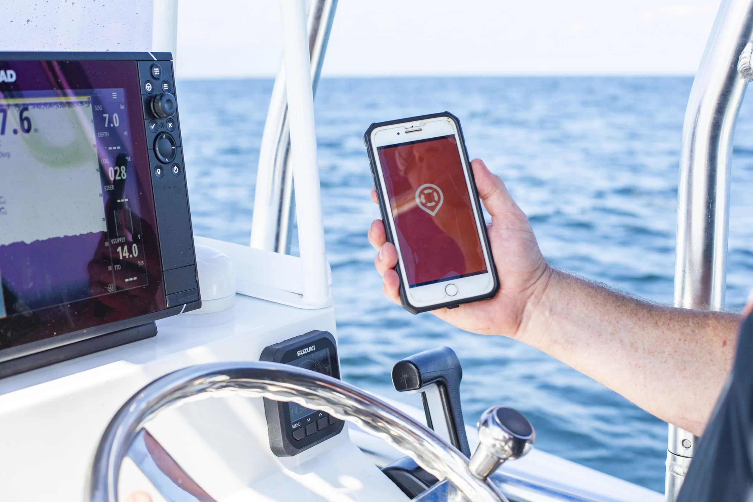 Person holding a smartphone with a GPS app on a boat, with a marine depth sounder display showing water depth and boat speed, and the open sea in the background.