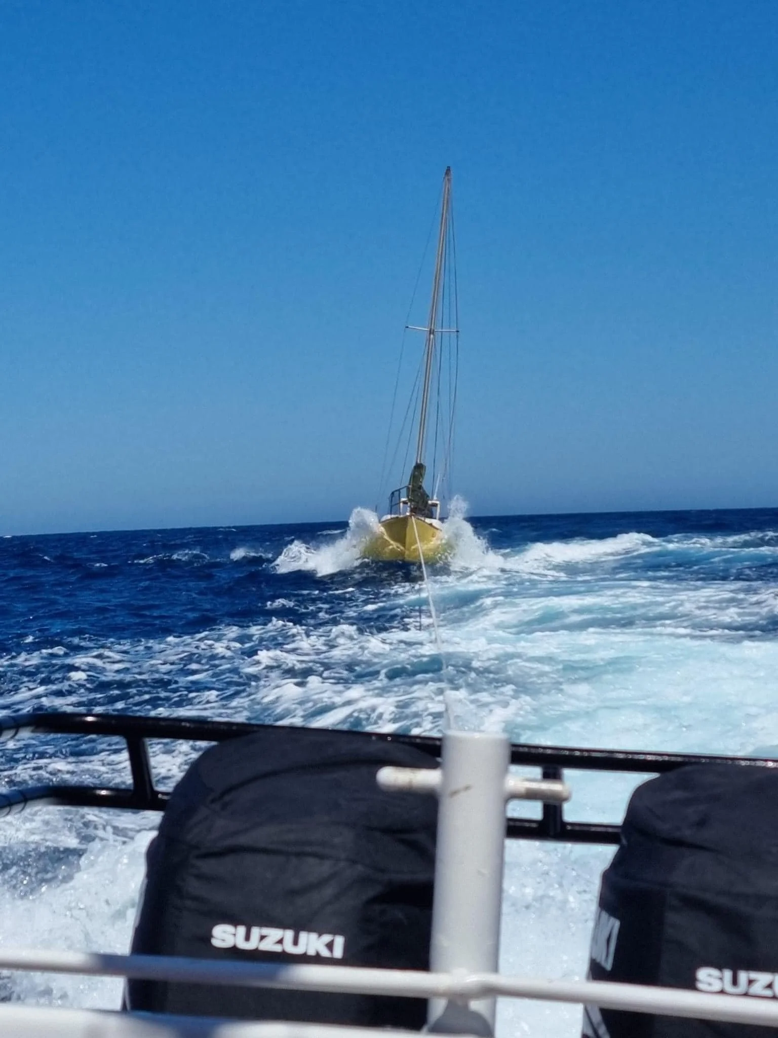 View from behind a boat with a Suzuki outboard motor, looking out over the water with another boat ahead. The sea is blue with white foam, and the sky is clear.