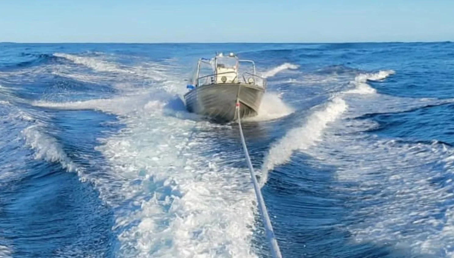 A boat moving through the open ocean, leaving a wake behind as it is pulled by a line.
