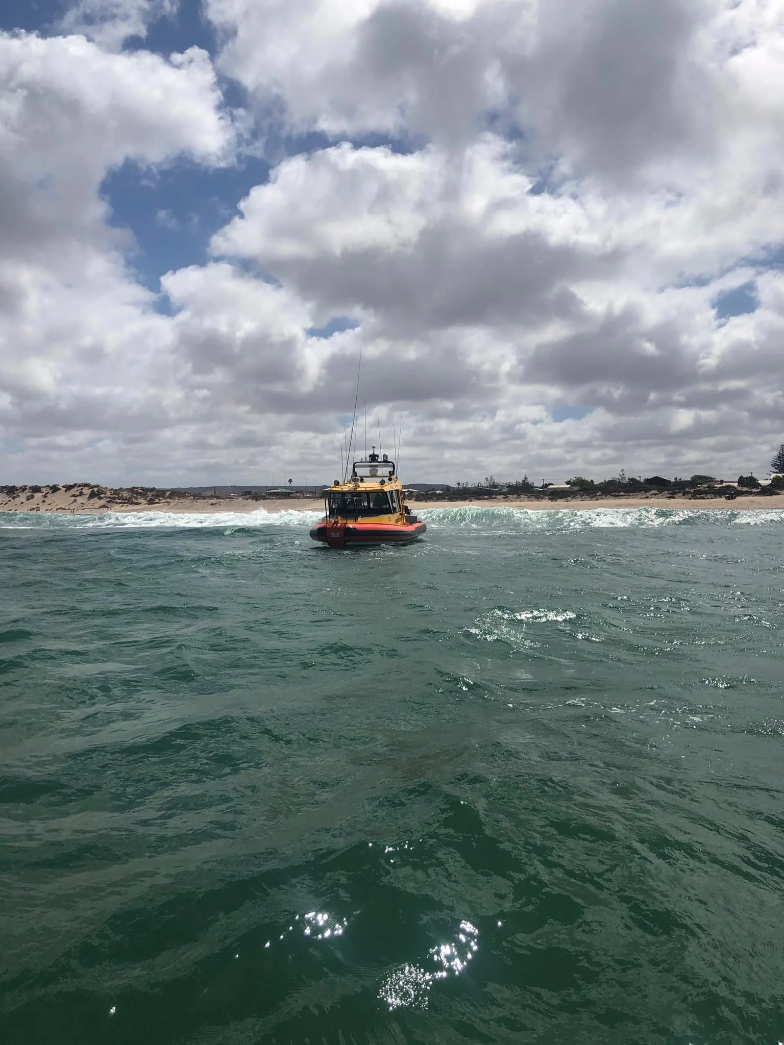 A yellow and black rescue boat on the ocean near the shoreline under a cloudy sky.
