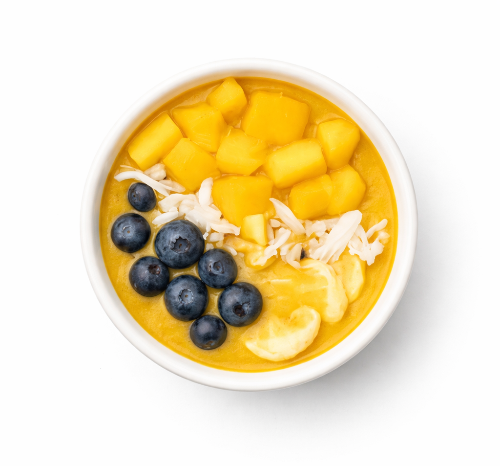 A bowl of mango and blueberry smoothie topped with shredded coconut and small chunks of mango.