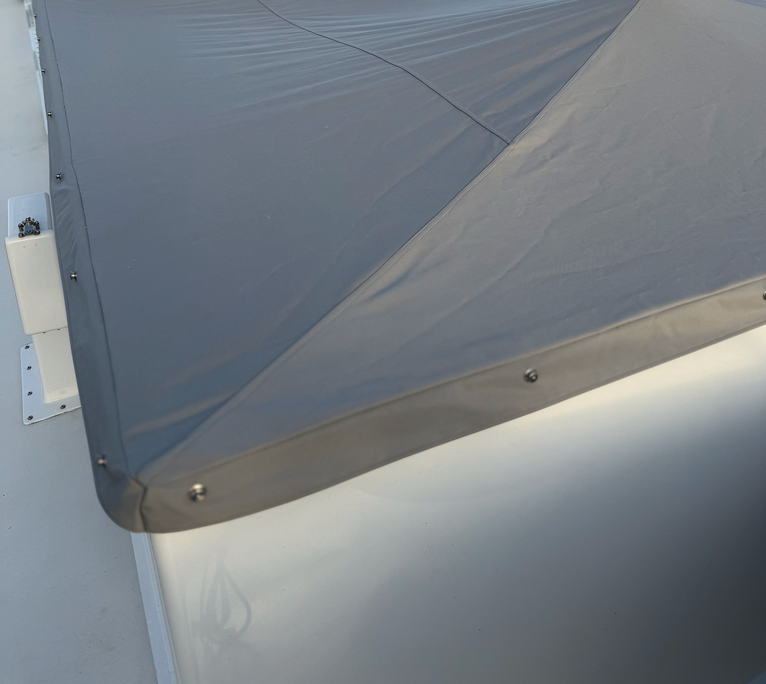 Close-up of a rooftop with a gray vent cover secured with screws, and a small white electrical box mounted on the surface.