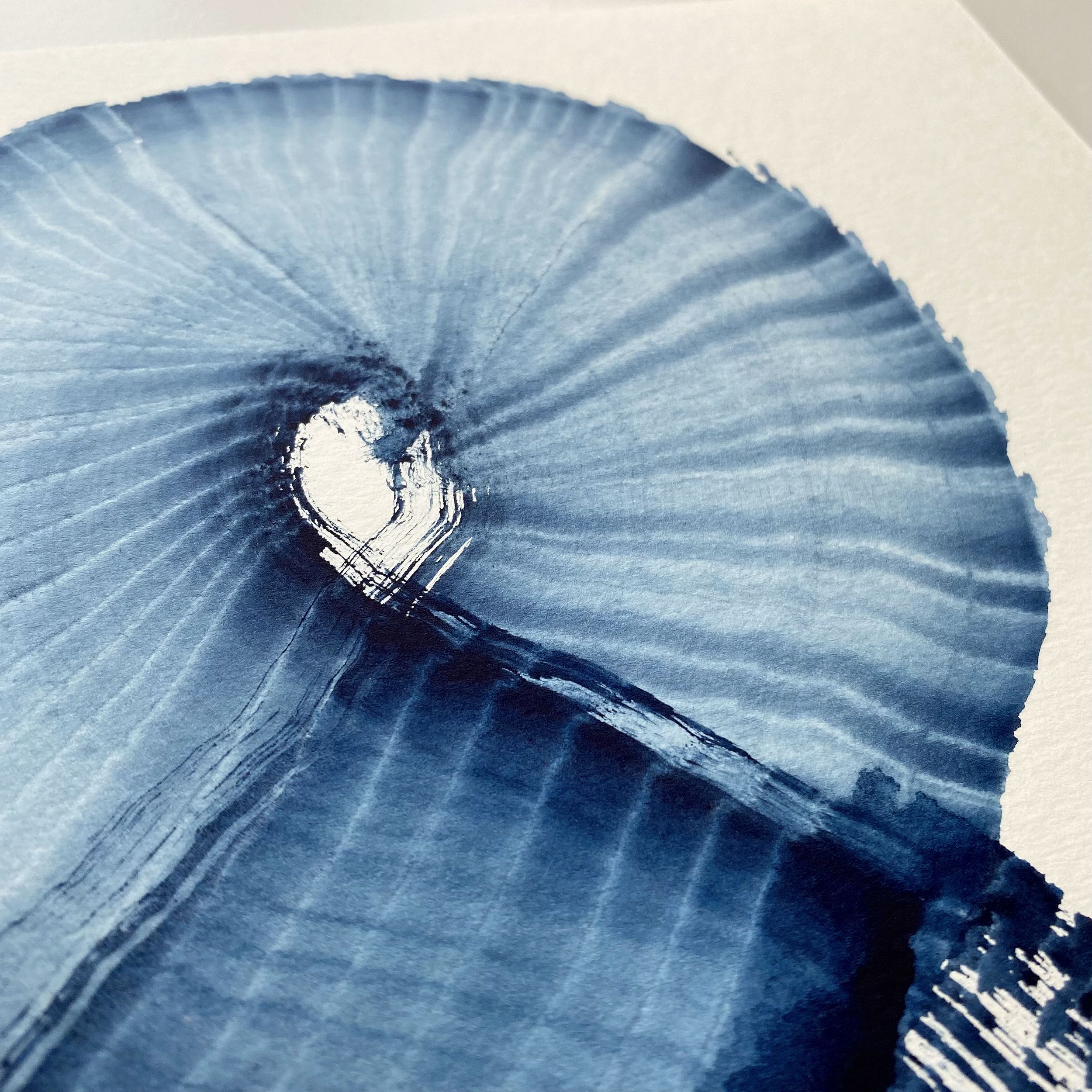 Close-up of a textured, circular, blue watercolor art piece with radiating lines and a central heart shape.