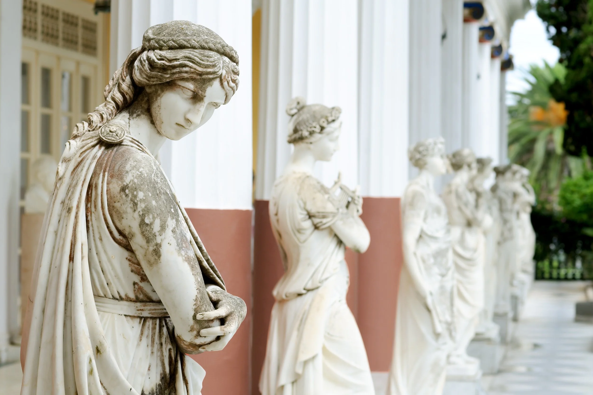 Row of ancient marble statues of Greek muses standing in a line outdoors.