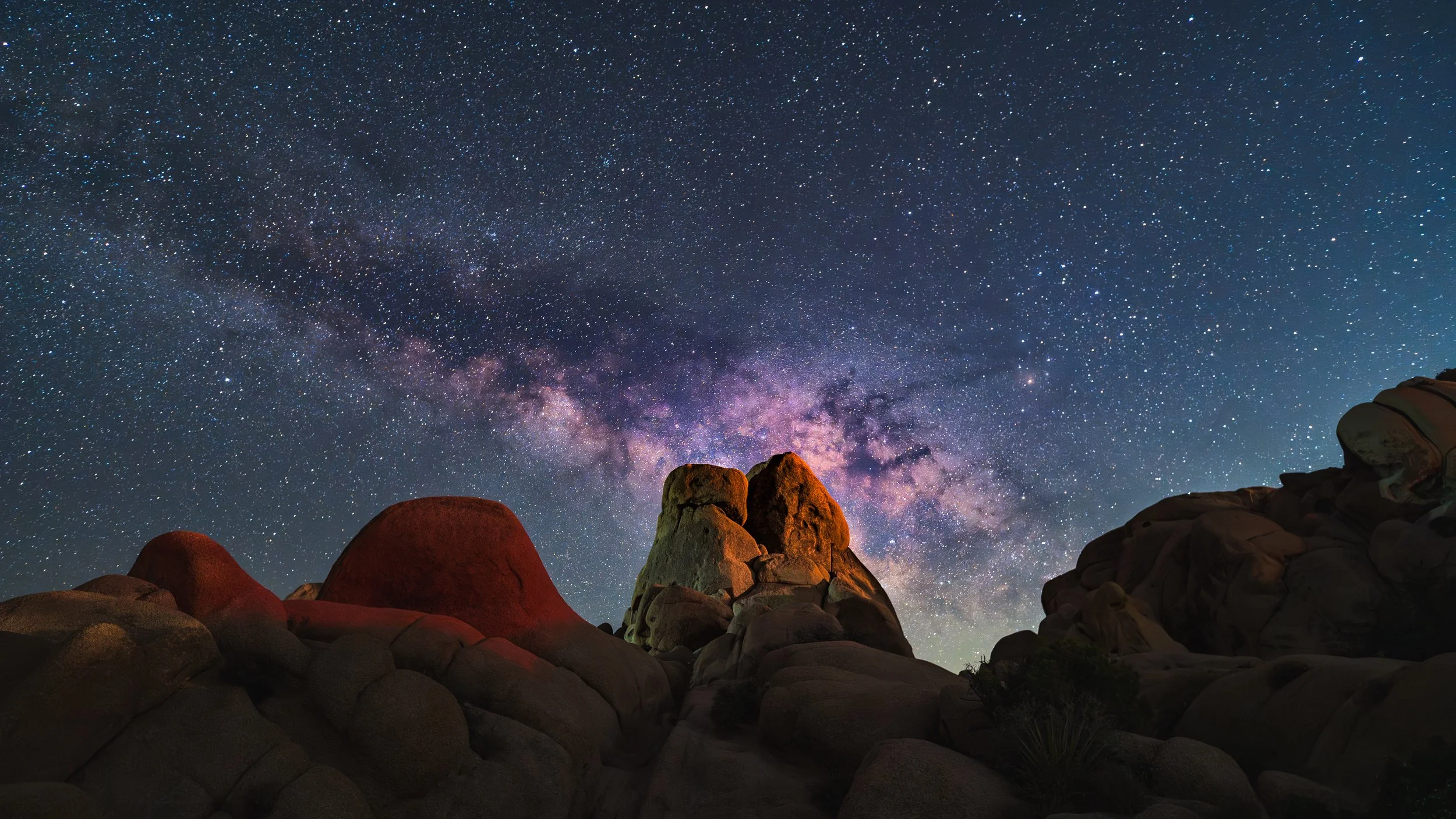 A starry night sky with the Milky Way galaxy visible above rocky formations.