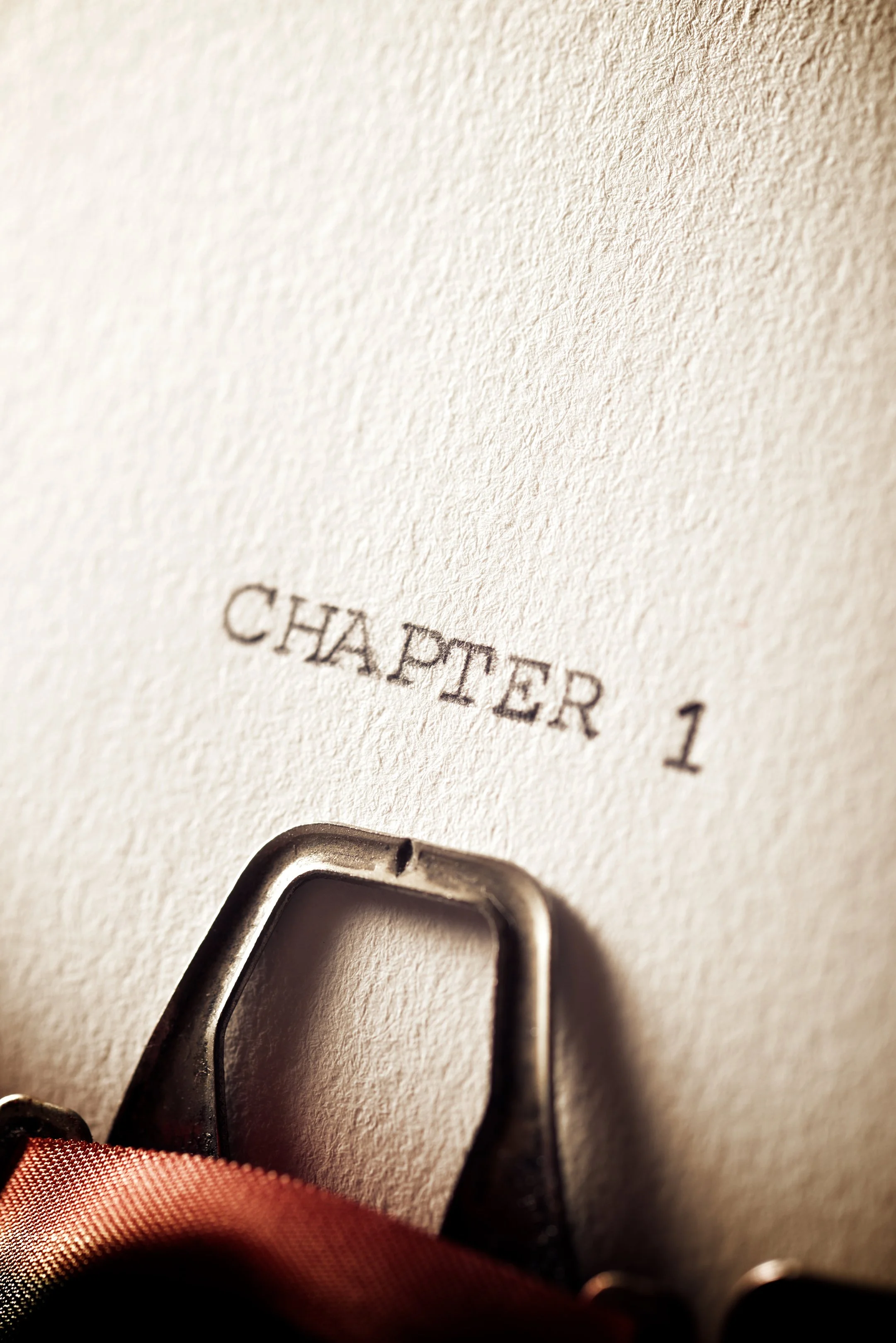 Close-up view of a typewriter and paper with text 'CHAPTER 1' and a part of the typewriter ribbon below the text.