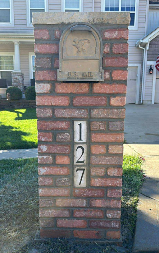 A brick mailbox with a metal mailbox on top, featuring an embossed bird and the words "U.S. Mail." Below the mailbox, the house number "127" is displayed with large black digits on white tiles.