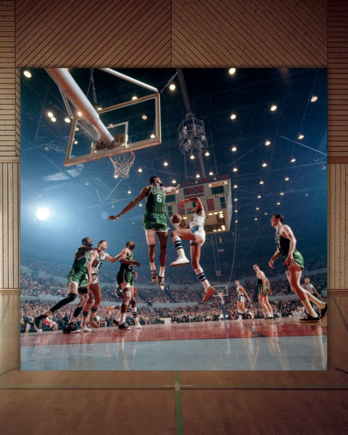 A basketball game in progress with players jumping near the hoop. Spectators are visible in the stands.
