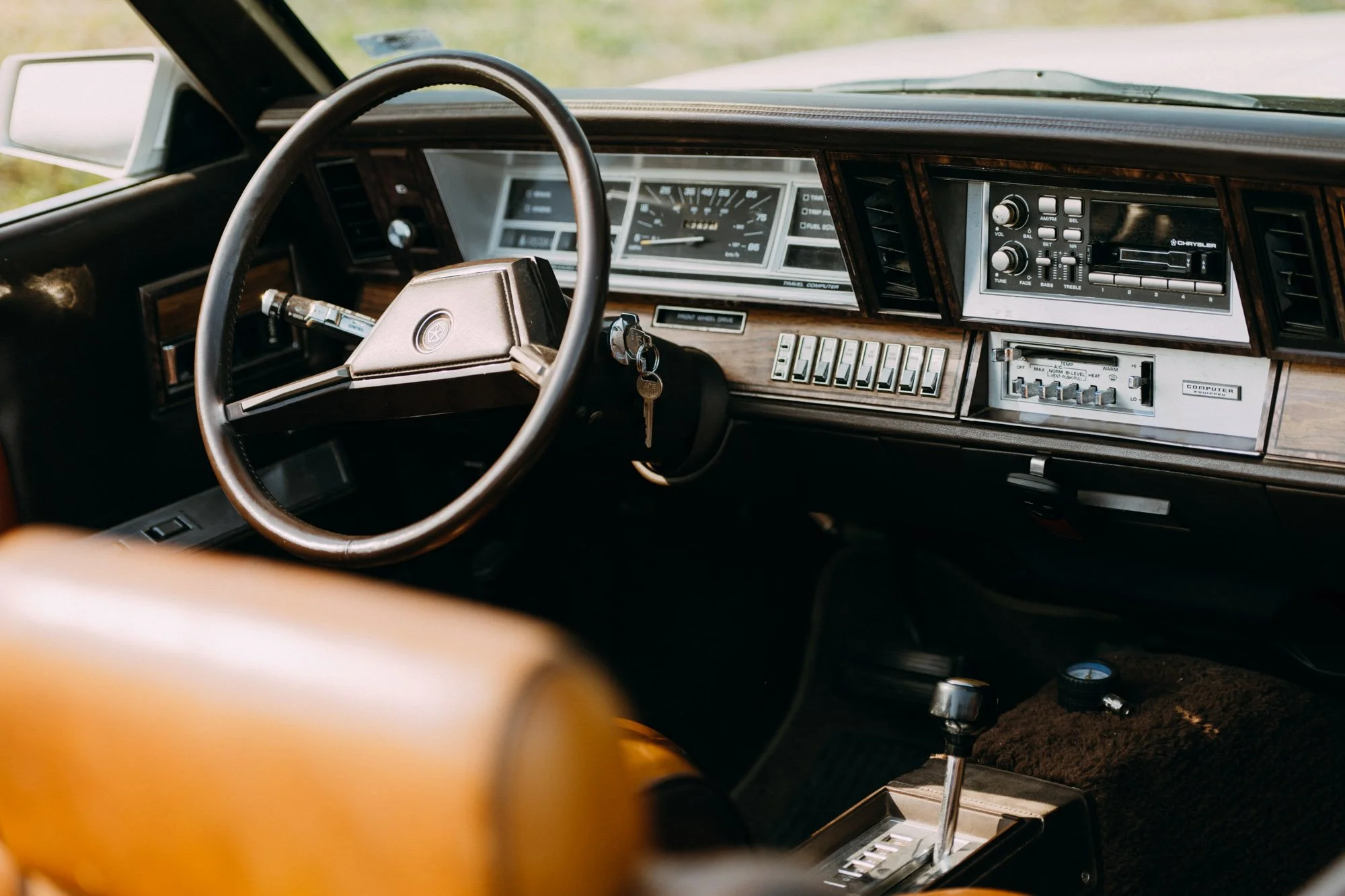 Interior of a vintage car showing a wooden dashboard, steering wheel, and radio controls, with a gear shift and key in ignition.
