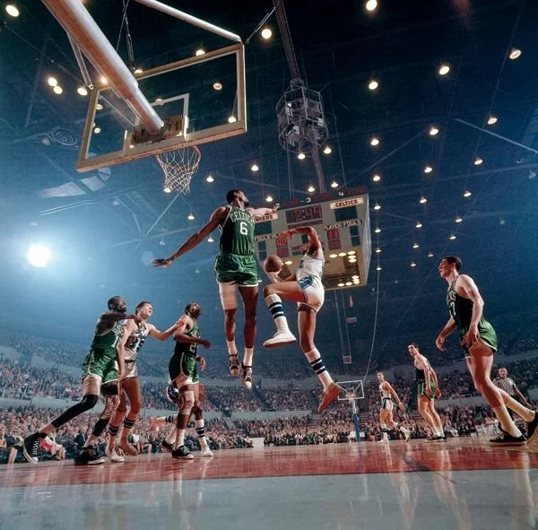 Basketball game with players jumping for the ball in an arena filled with spectators.