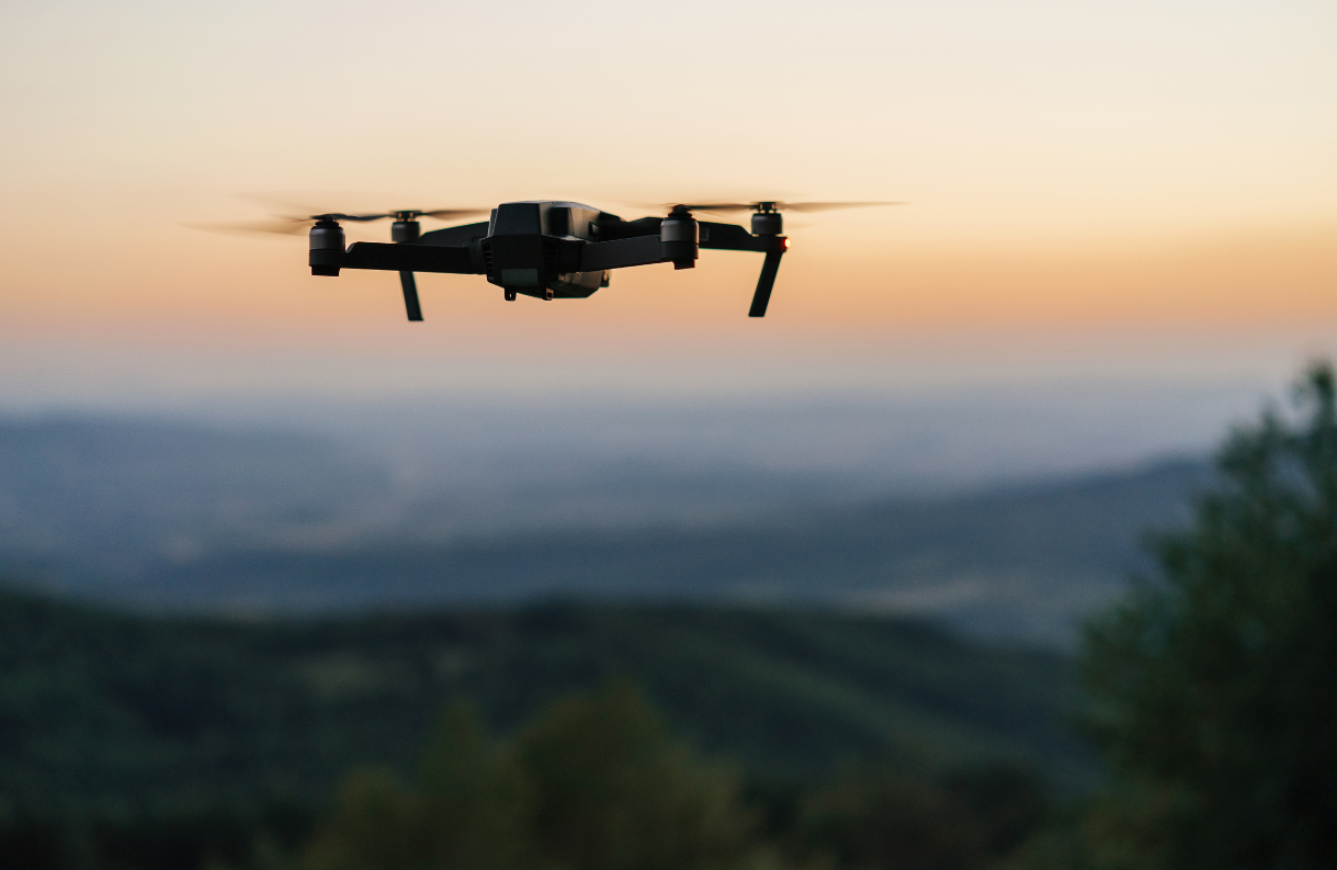 A drone flying in the sky at sunset over a landscape with rolling hills and trees.