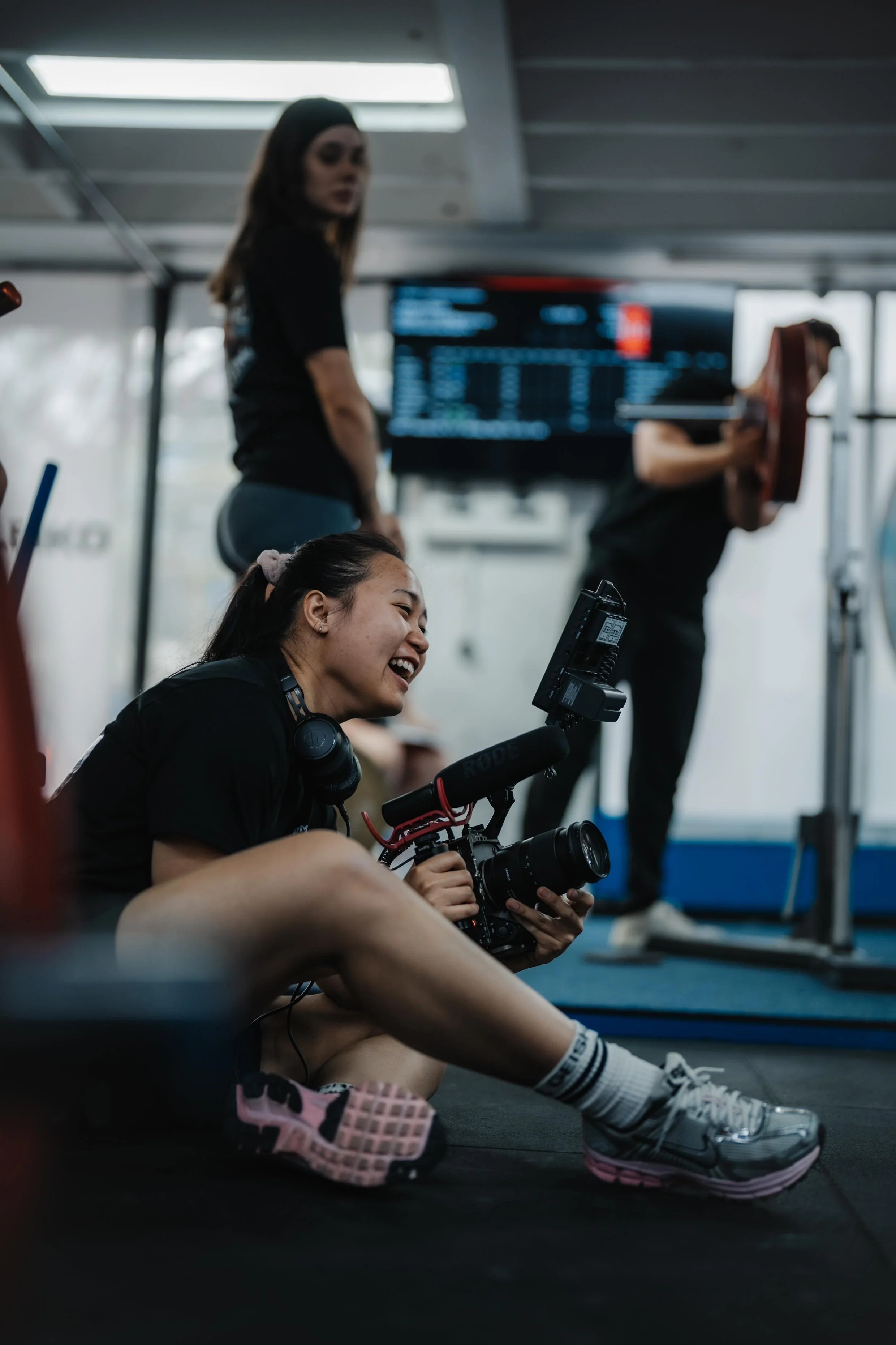 Women recording a video at a gym, with others working out in the background.