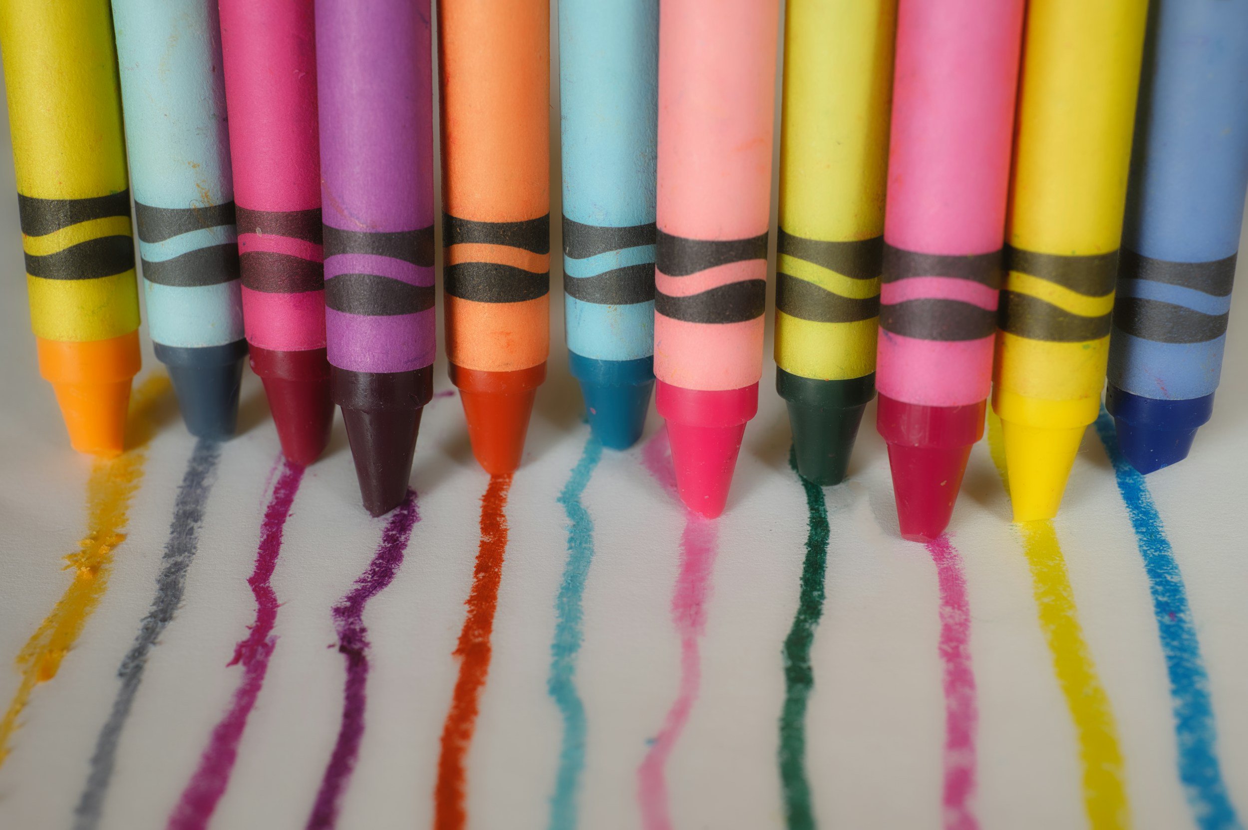 Colorful crayons aligned on paper, with colorful lines drawn beneath each crayon.