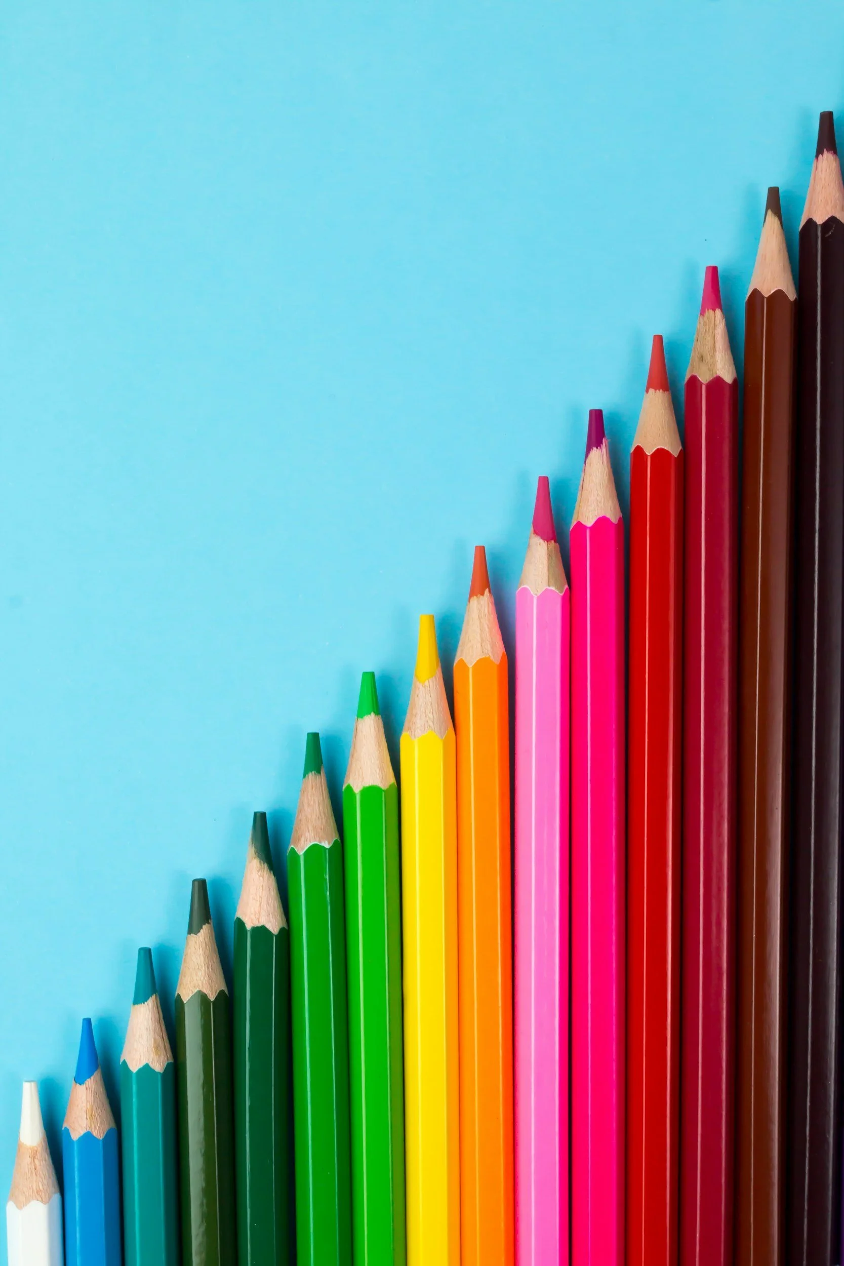 Colorful colored pencils arranged from smallest to largest on a blue background.
