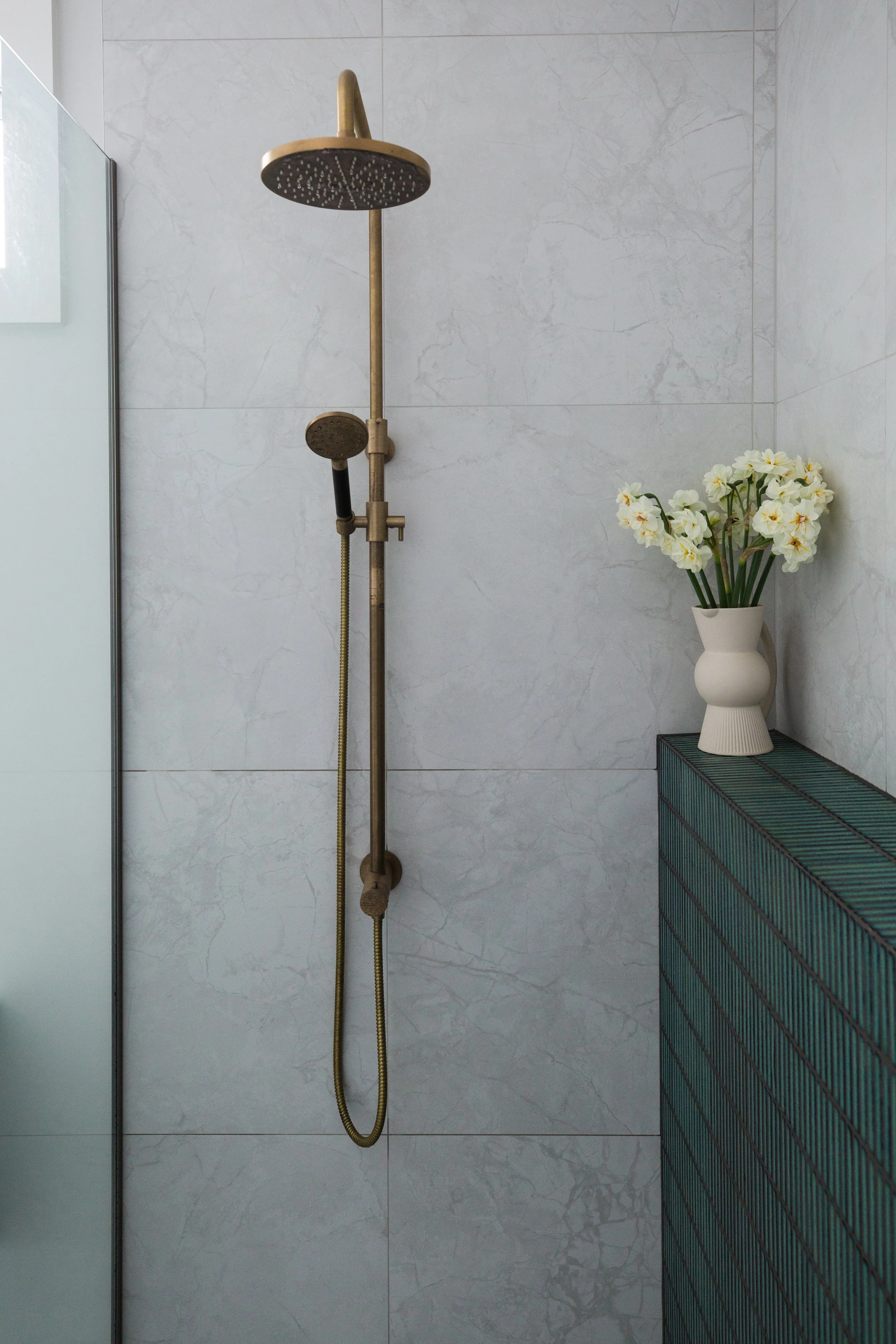 Bathroom shower with two showerheads and a white vase with flowers on a teal cabinet.