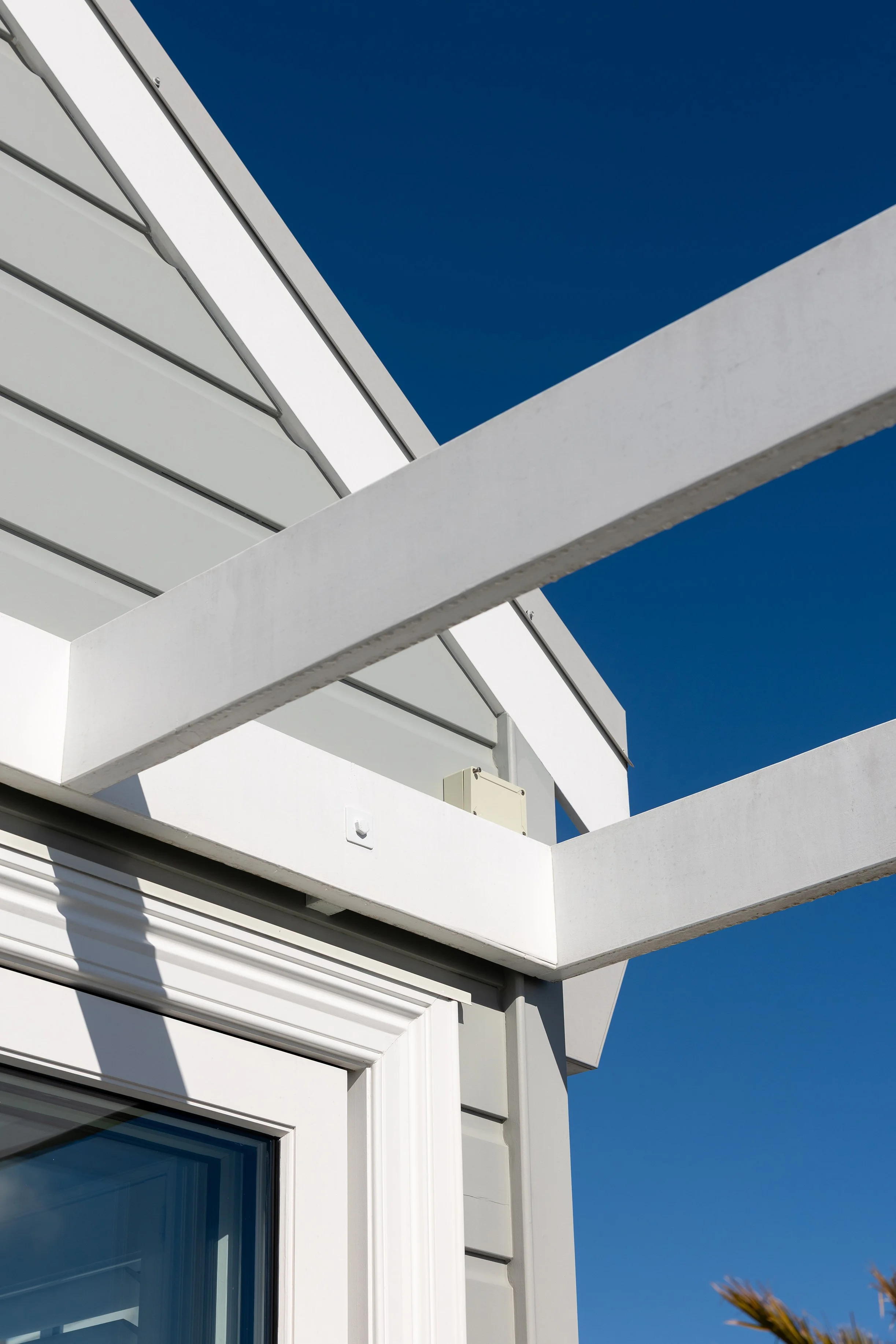 Close-up of a modern white building with angular architectural design, featuring large glass windows and white horizontal beams against a clear blue sky.