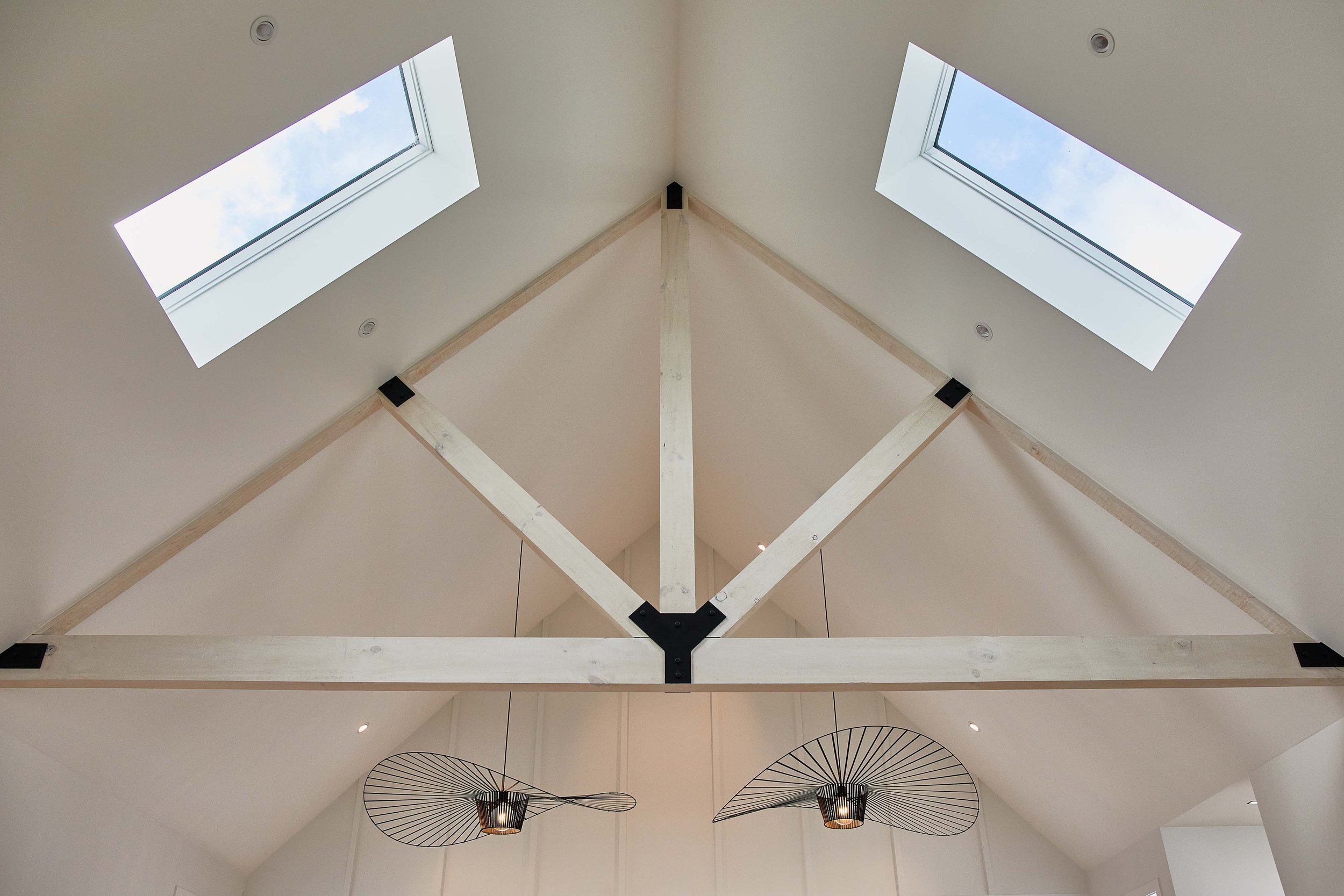 Interior view of a room with a ceiling structure, two skylights in the sloped ceiling, and hanging light fixtures with wireframe shades.