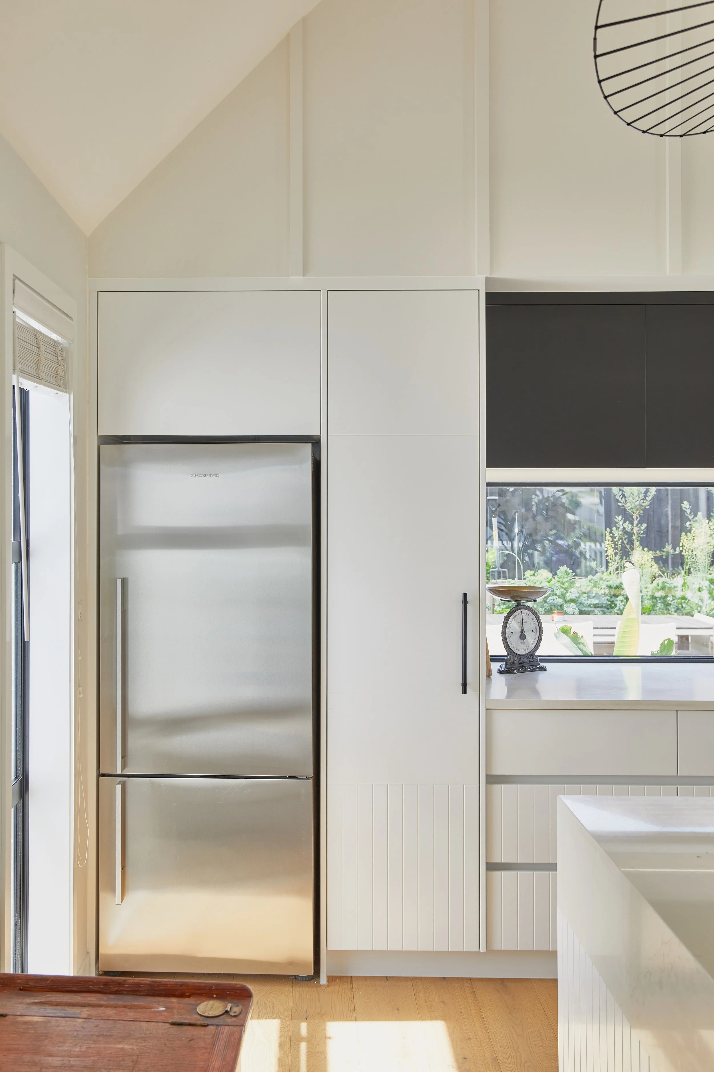 Modern kitchen with white cabinets, a stainless steel refrigerator, and a window overlooking a garden.