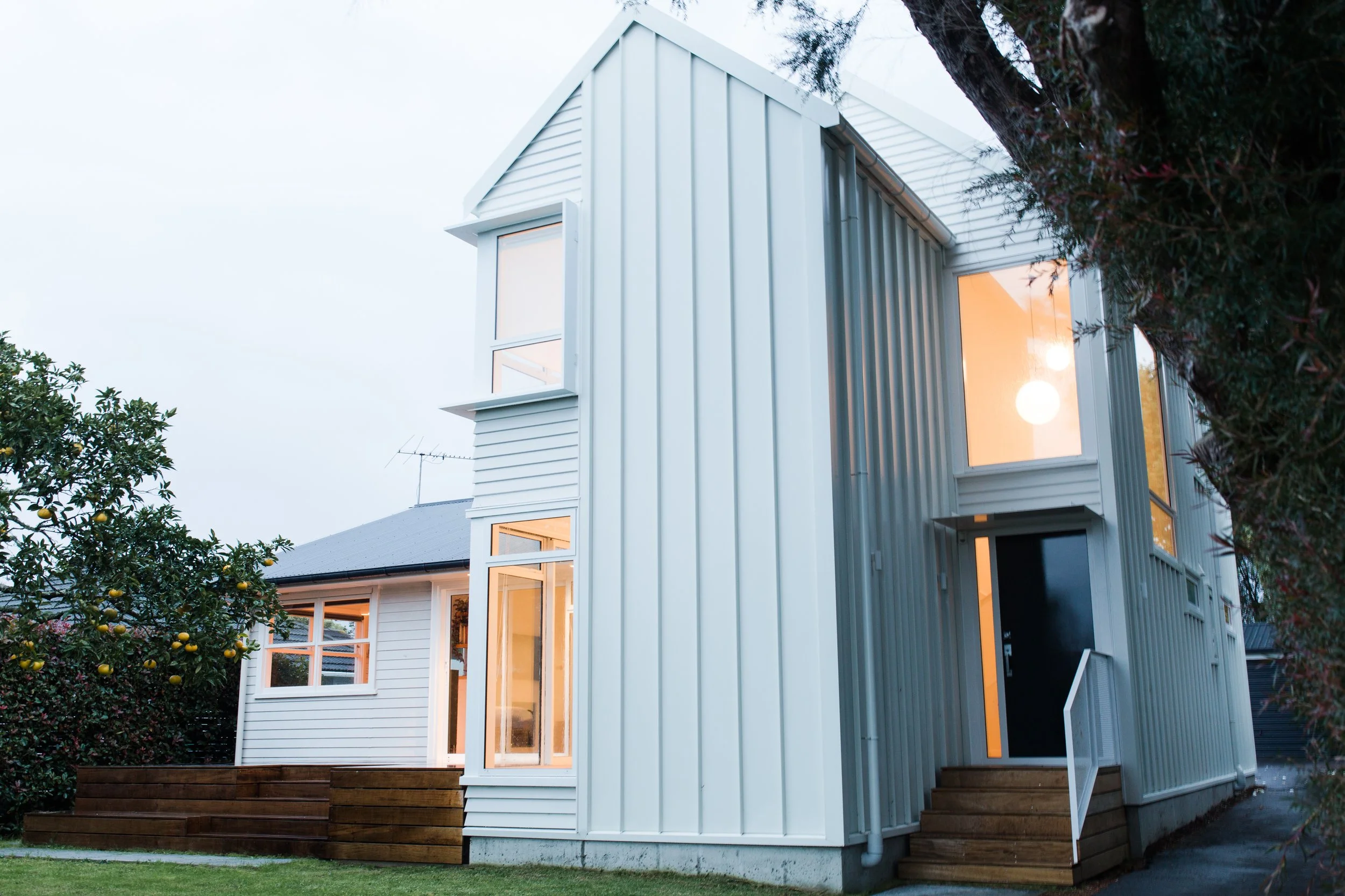 Modern two-story house with white siding and large windows, surrounded by greenery, with steps leading to the front door