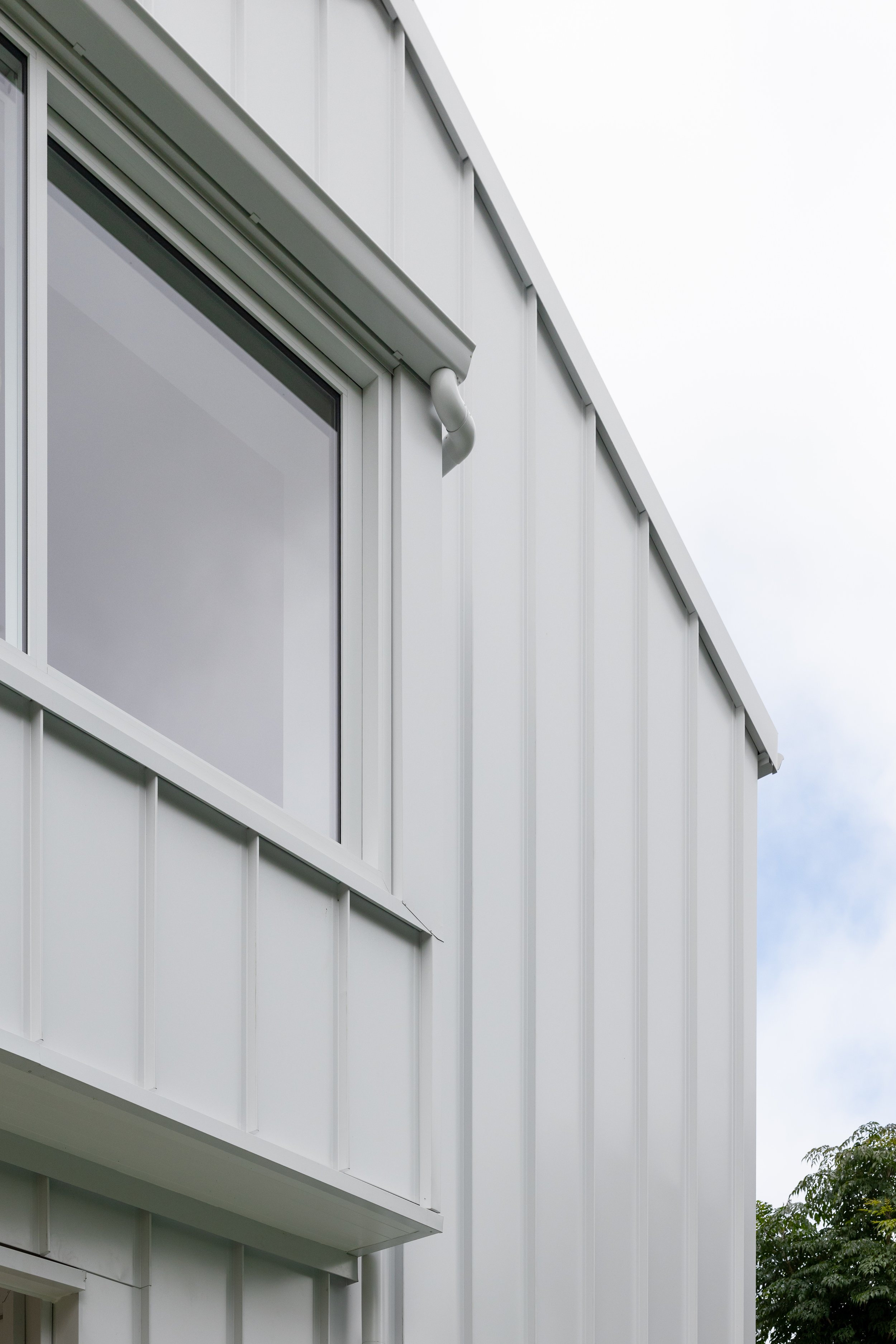 Close-up view of a white metal building exterior with a large window and a rain gutter.