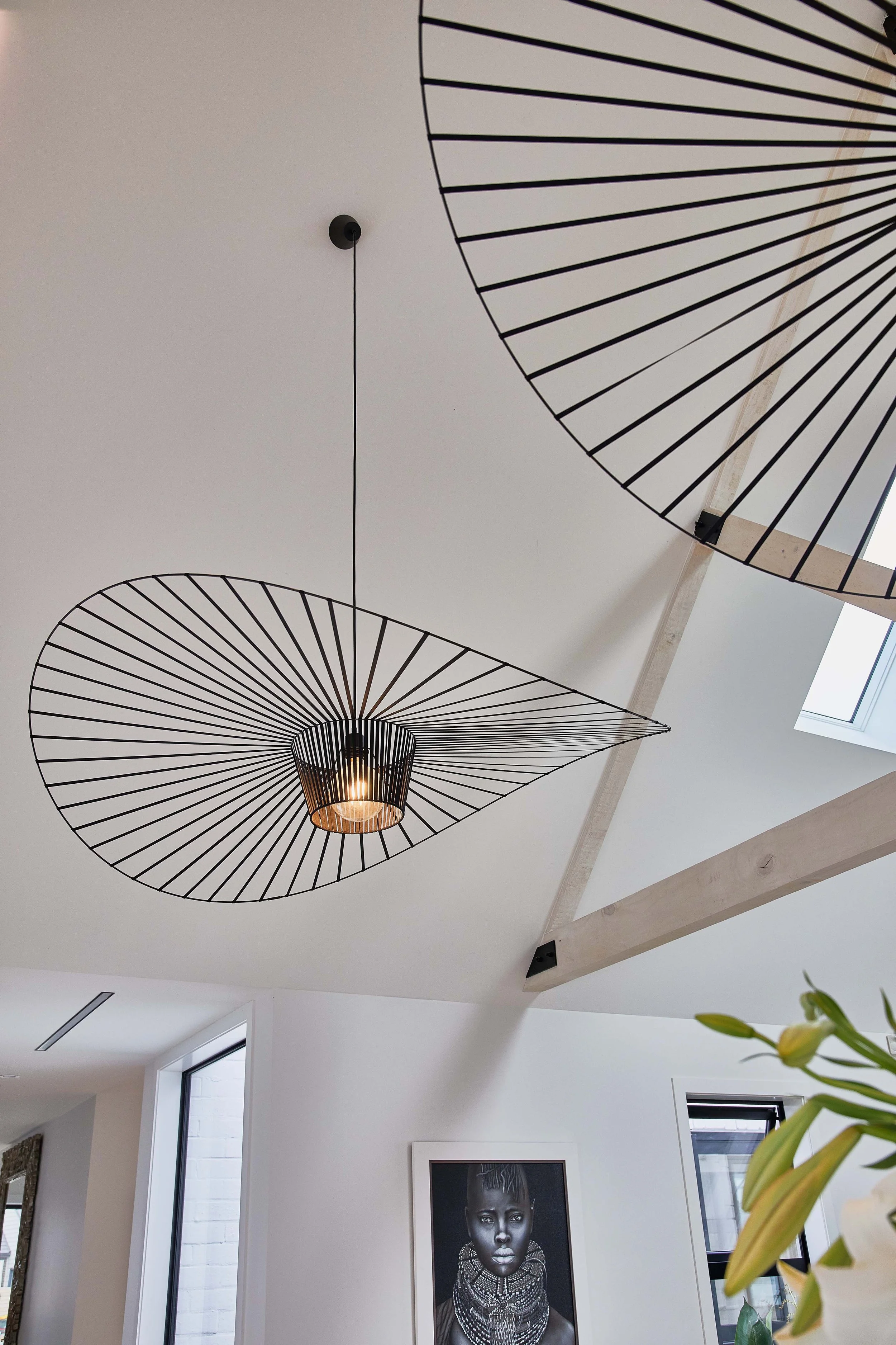 Modern pendant light fixture with black wireframe design hanging from the ceiling in a bright, minimalist interior.